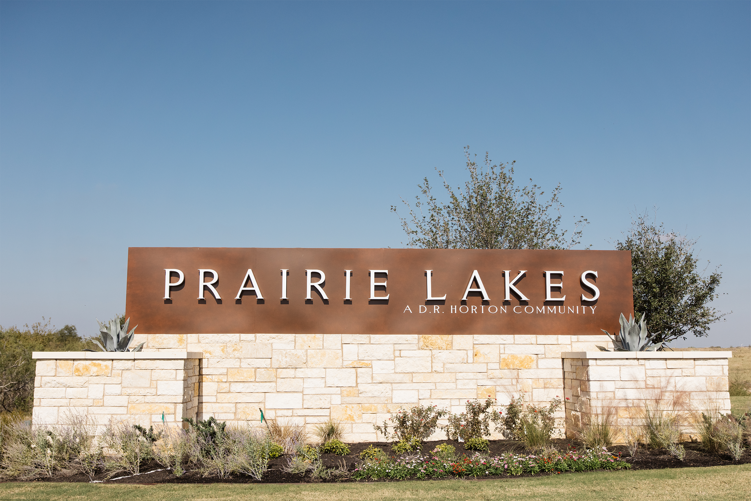 Entrance sign for Prairie Lakes, a D.R. Horton community, with landscaping and clear sky background.