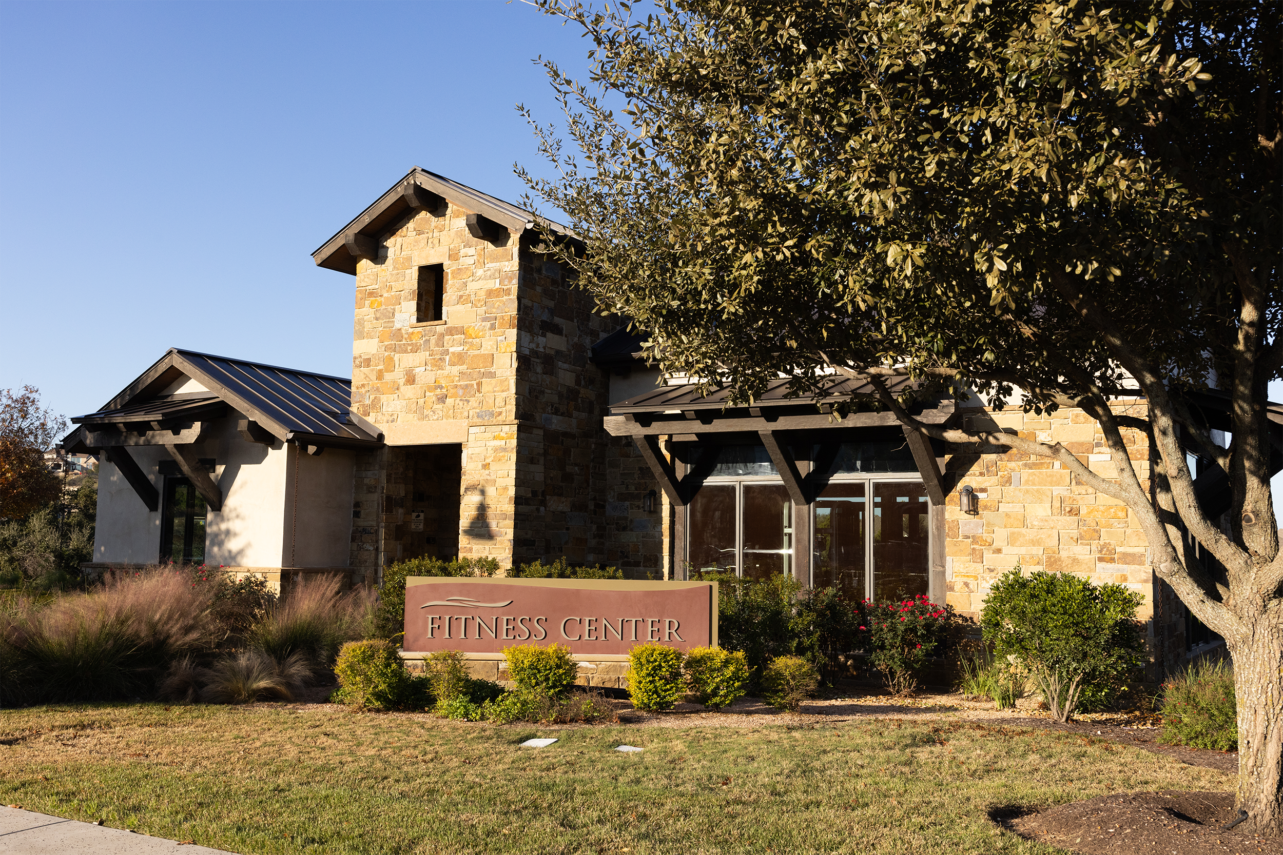 Stone building labeled 'Fitness Center' surrounded by trees and greenery under a clear blue sky.