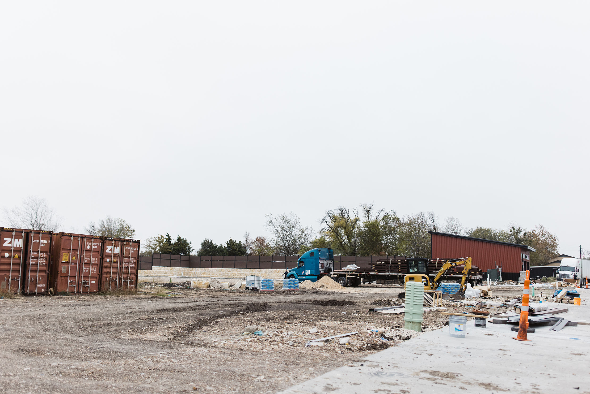 Construction site with containers, blue truck, excavator, and various materials.