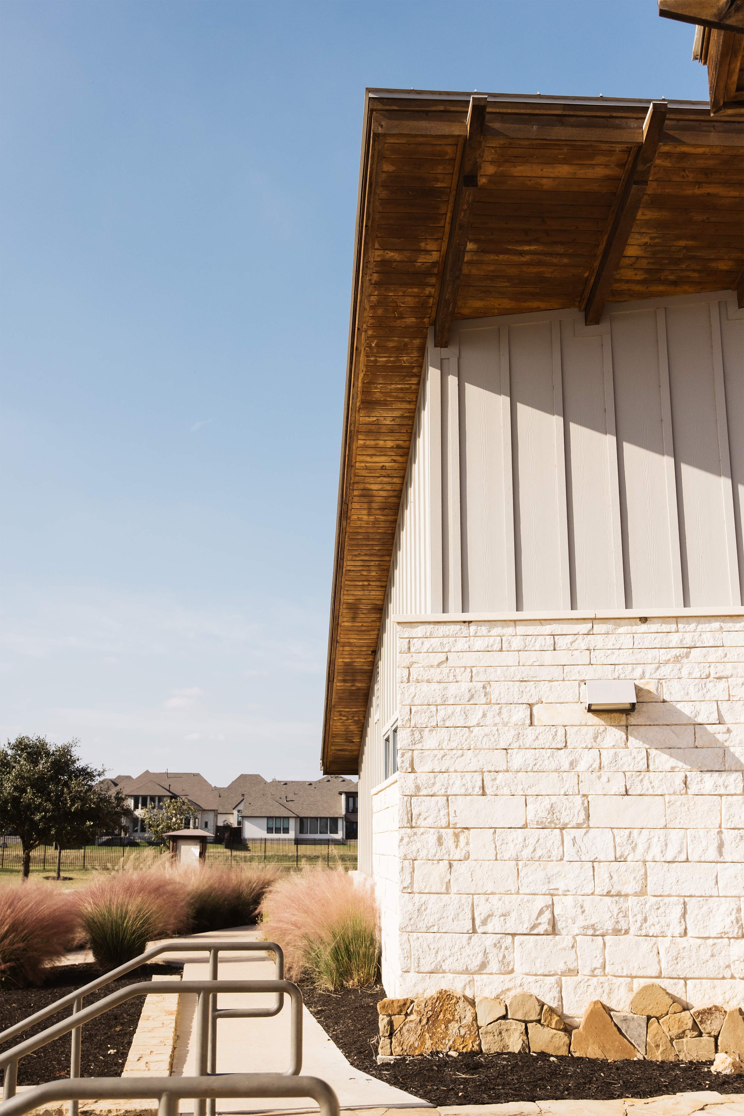 Modern building with stone wall and wooden roof, surrounded by landscaping, under a clear blue sky.