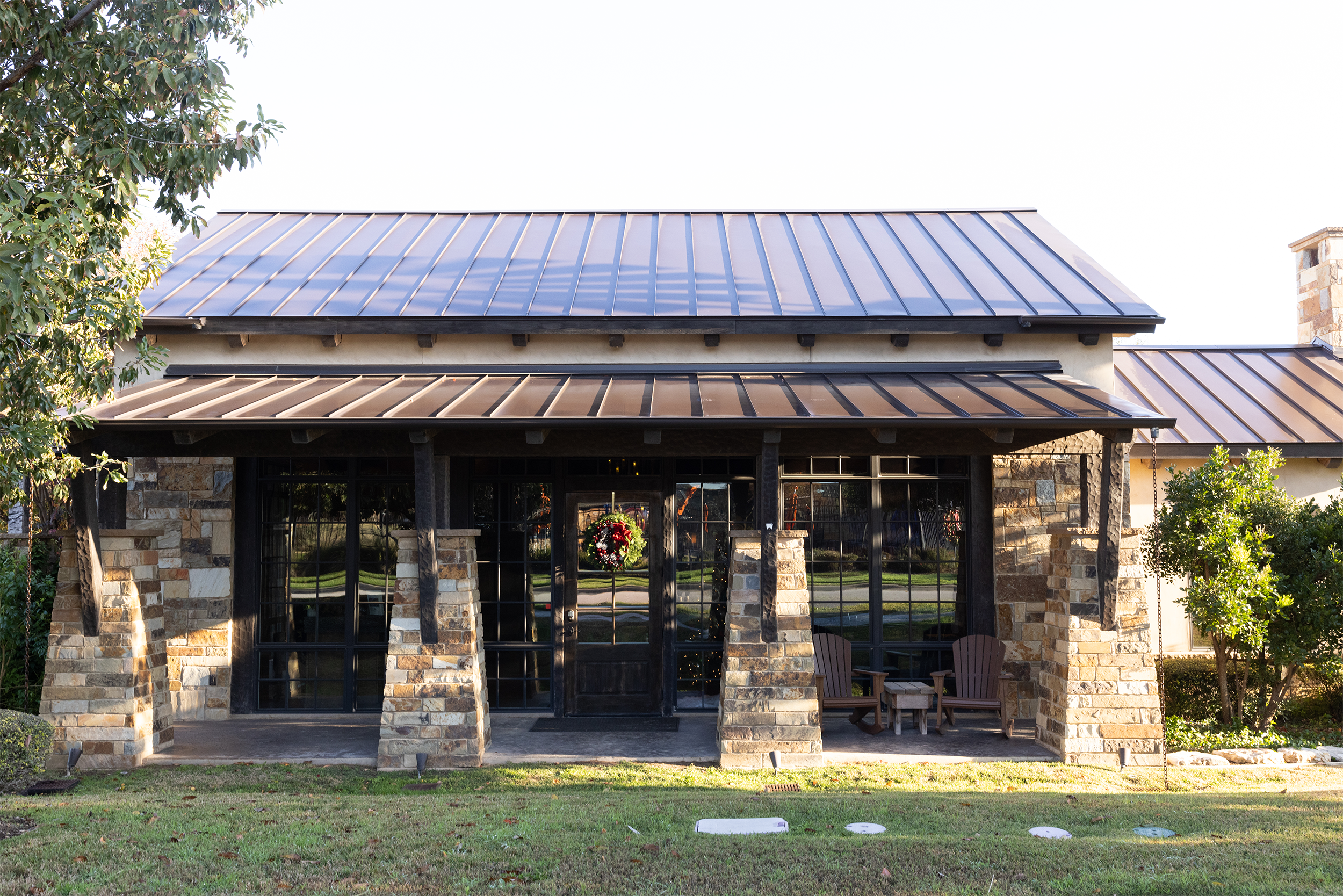 Stone exterior building with metal roof, patio chairs, and Christmas wreath on the door.