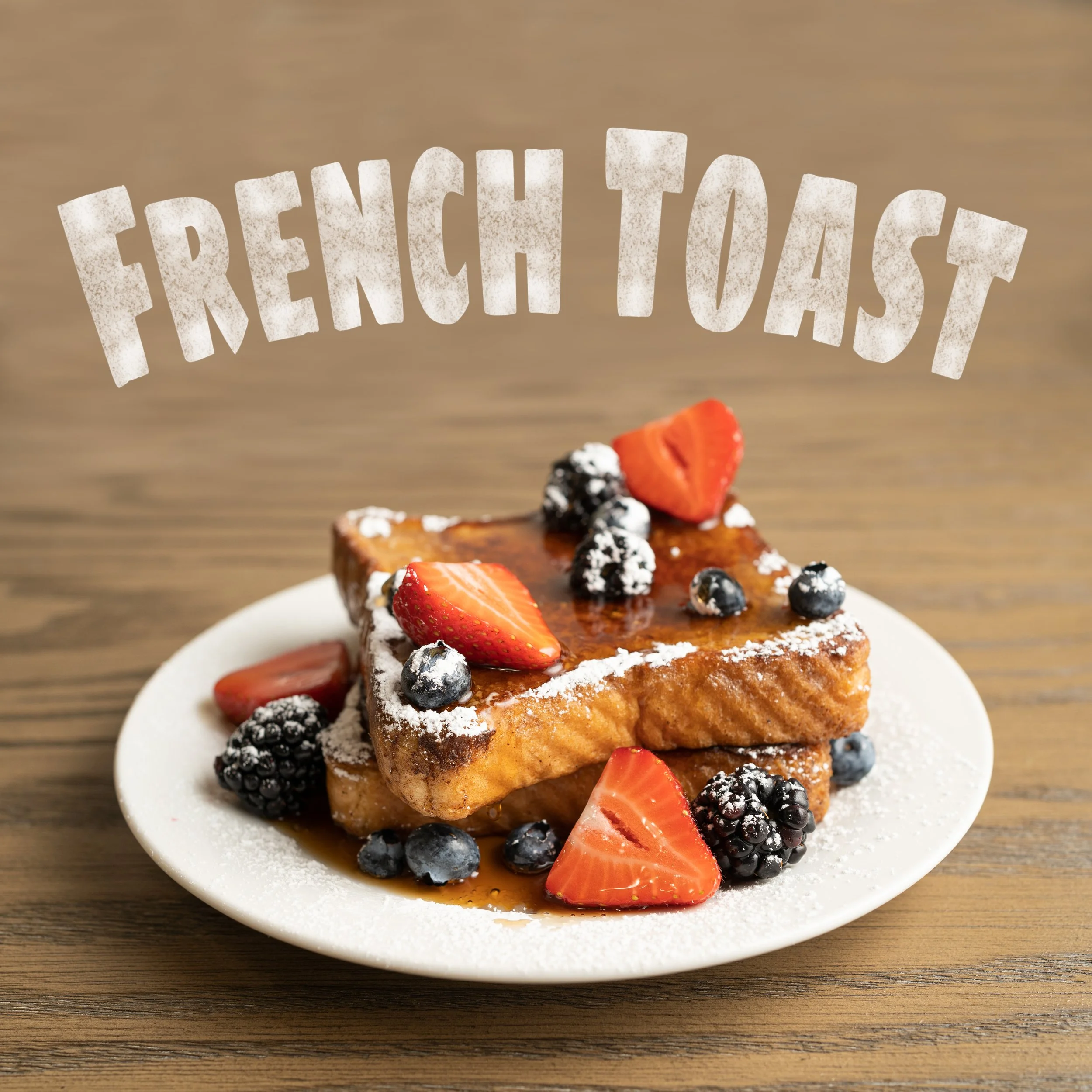 A dessert cake topped with fresh strawberries, blueberries, blackberries, and a dusting of powdered sugar, on a white plate on a wooden table.