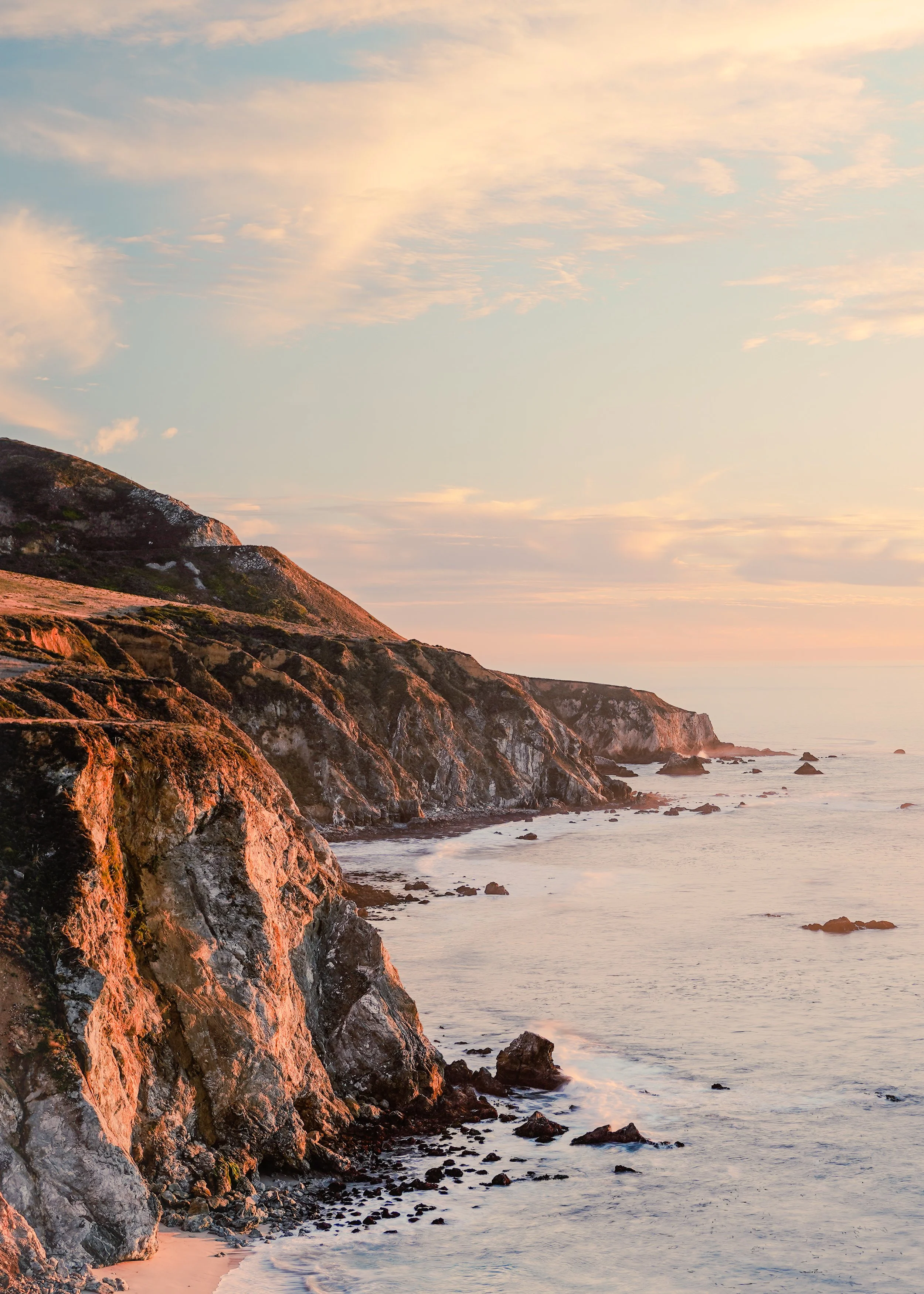 Cliffs along a rocky shoreline at sunset with a partly cloudy sky.