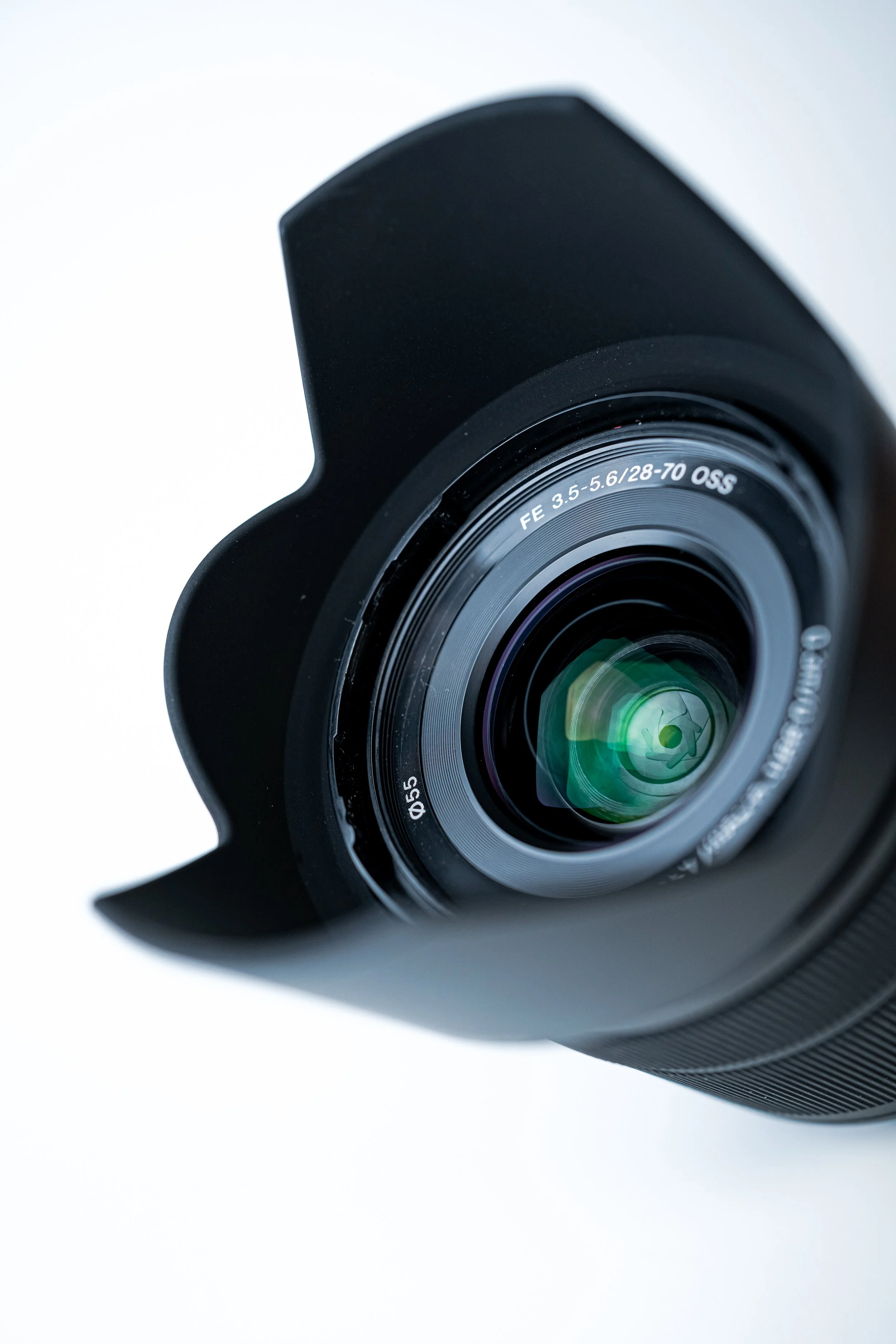 Close-up of a camera lens, with text indicating it is a 28-70mm zoom lens, attached to a black camera body with a lens hood.