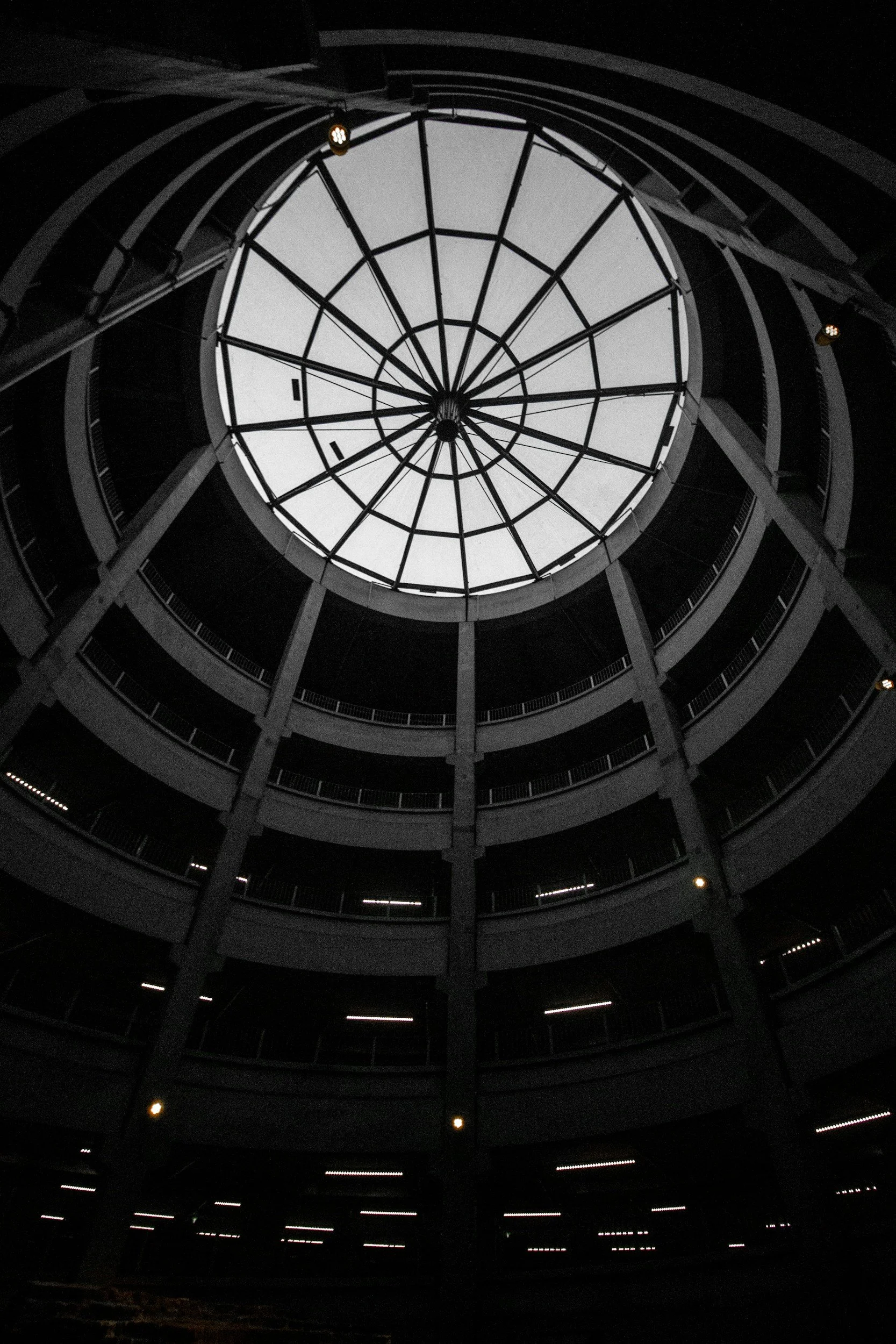 View looking up through the center of a circular multi-story parking garage with a large glass dome at the top, showing the sky above.