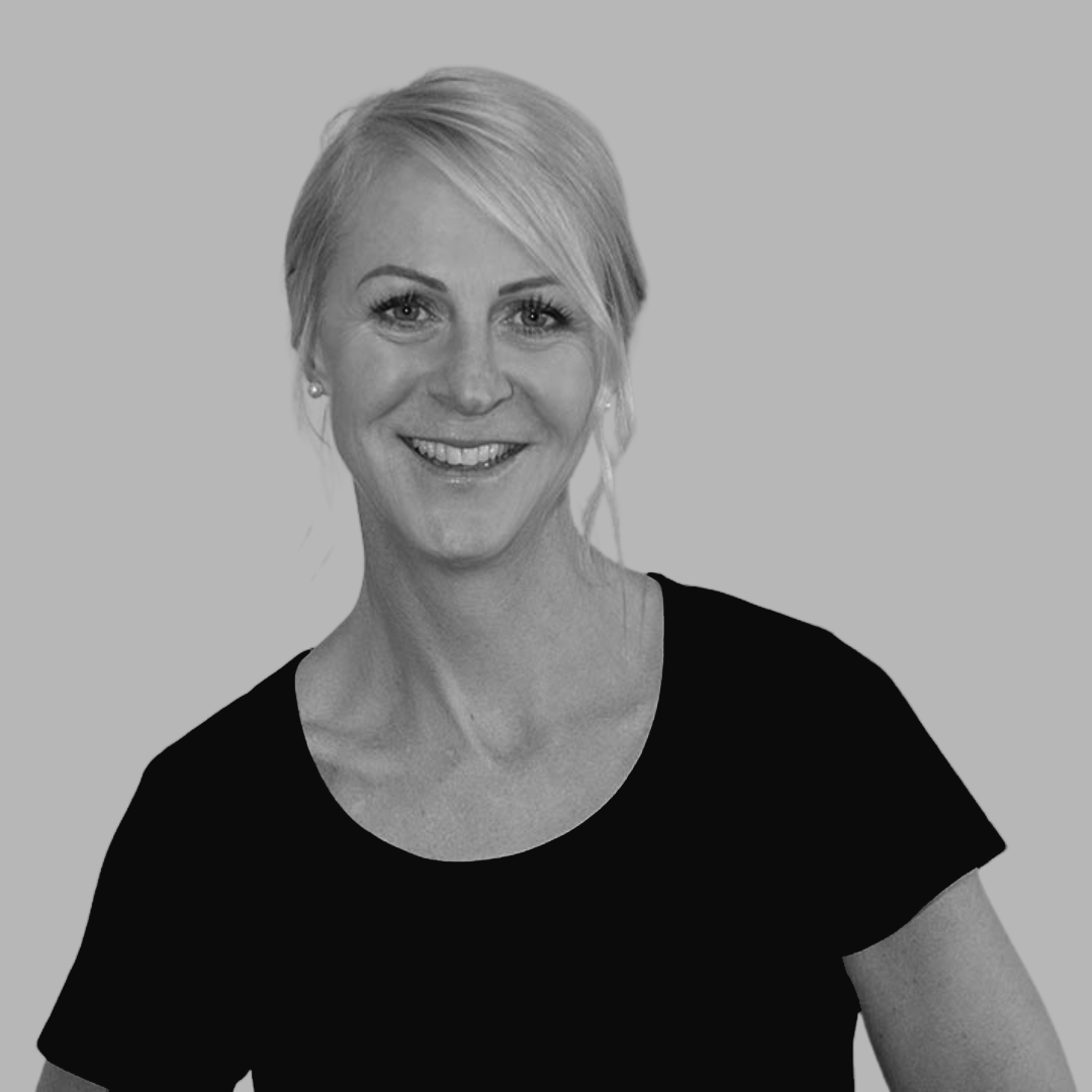 Black and white portrait of a smiling woman with short blonde hair, wearing a black top, looking directly at the camera.