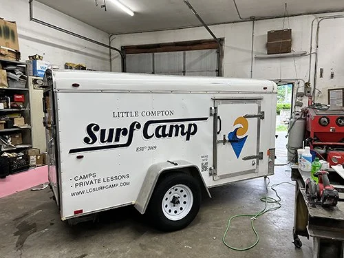 White enclosed trailer with vinyl wrap graphics and logo, parked inside a workshop garage