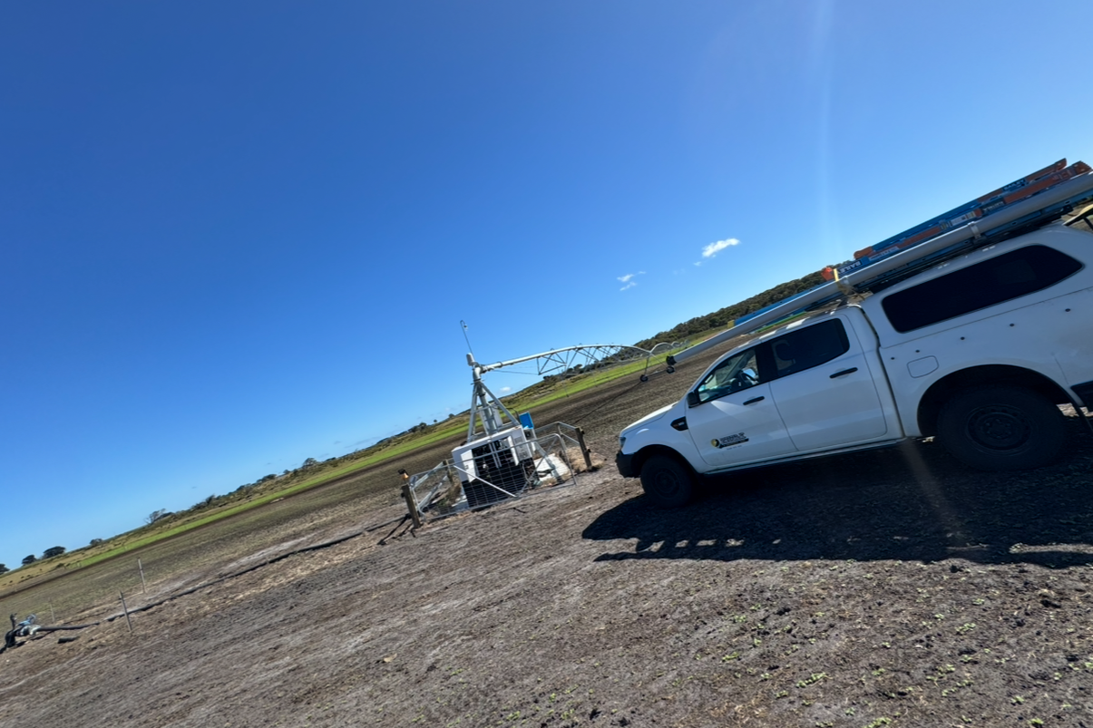 A white utility with equipment on top parked next to an irrigation system in a field under a clear blue sky.