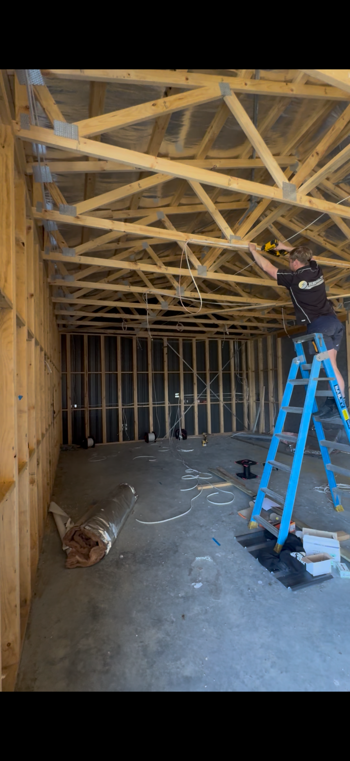 An electrician standing on a blue ladder roughing in electrical cable on a new build.