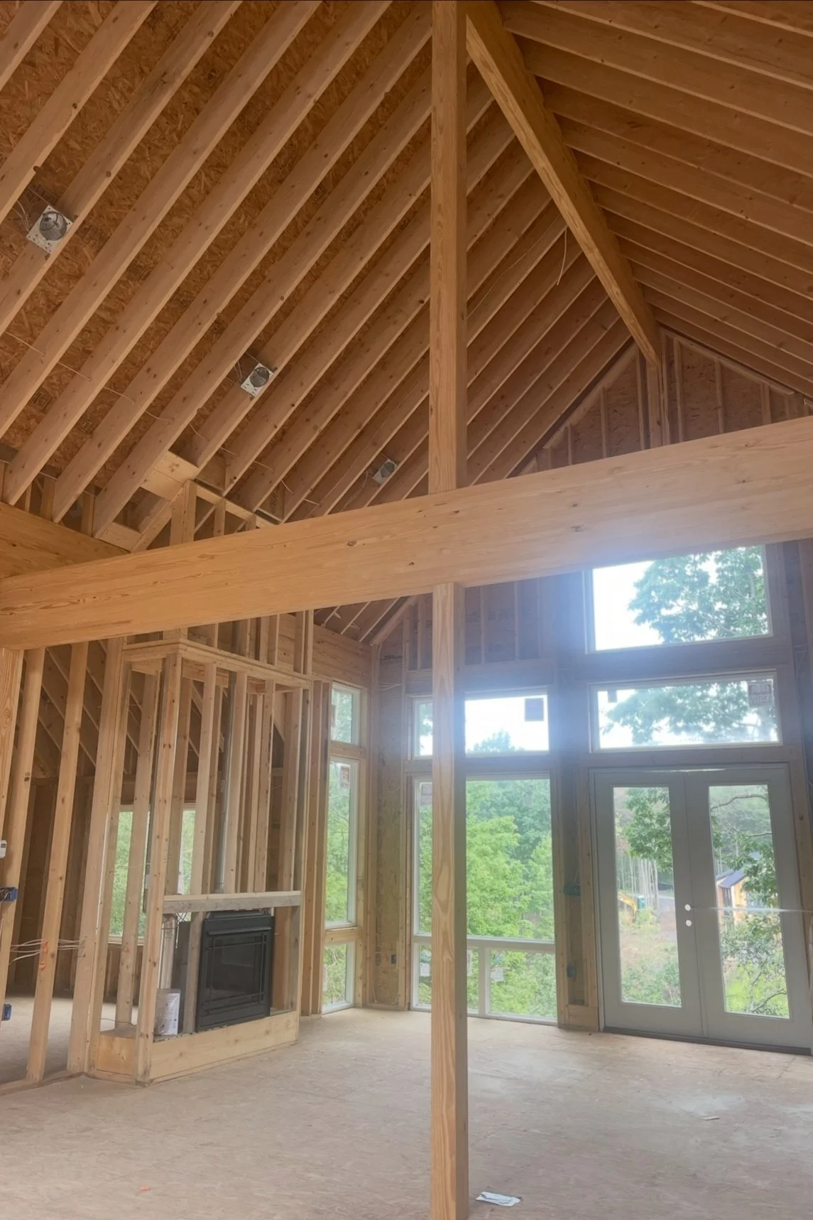 Interior of a house under construction with exposed wooden framing, large windows, and a vaulted ceiling.