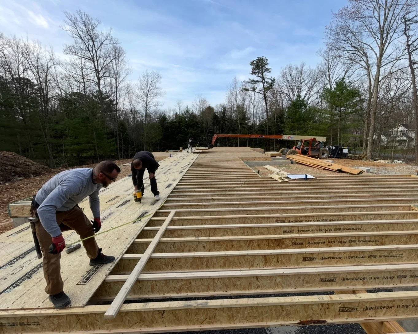 Construction workers installing framing for a building deck outdoors with trees in the background.