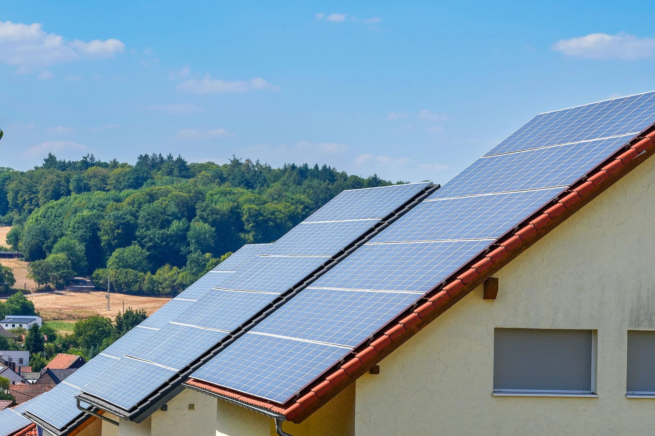 Solar panels installed on the roof of a house with a background of green trees and blue sky.