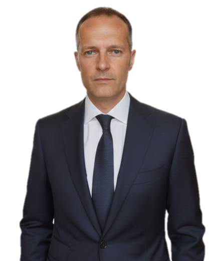 A man in a dark blue suit, white shirt, and navy tie standing against a plain background.
