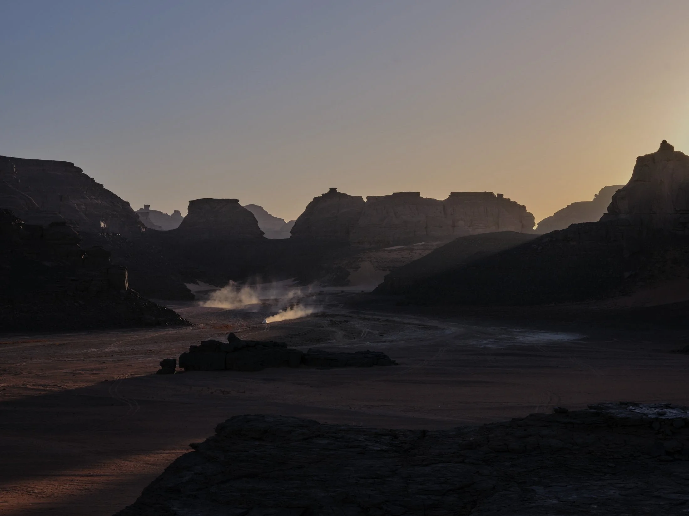 A desert landscape at sunset with large rock formations and steam rising from the ground.