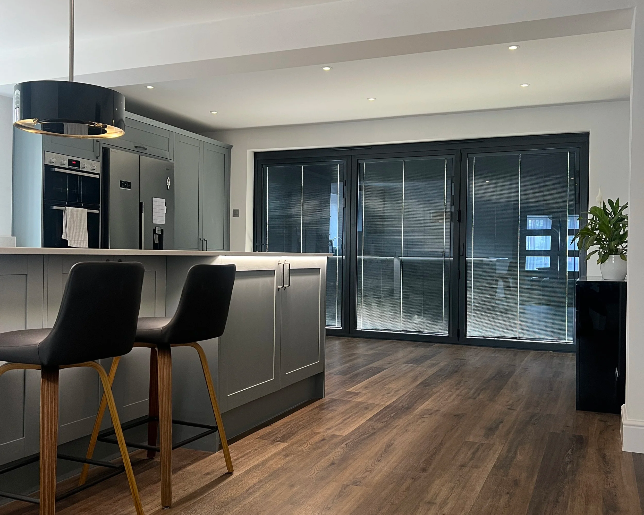 Modern kitchen refit with grey cupboards and black bar stools.
