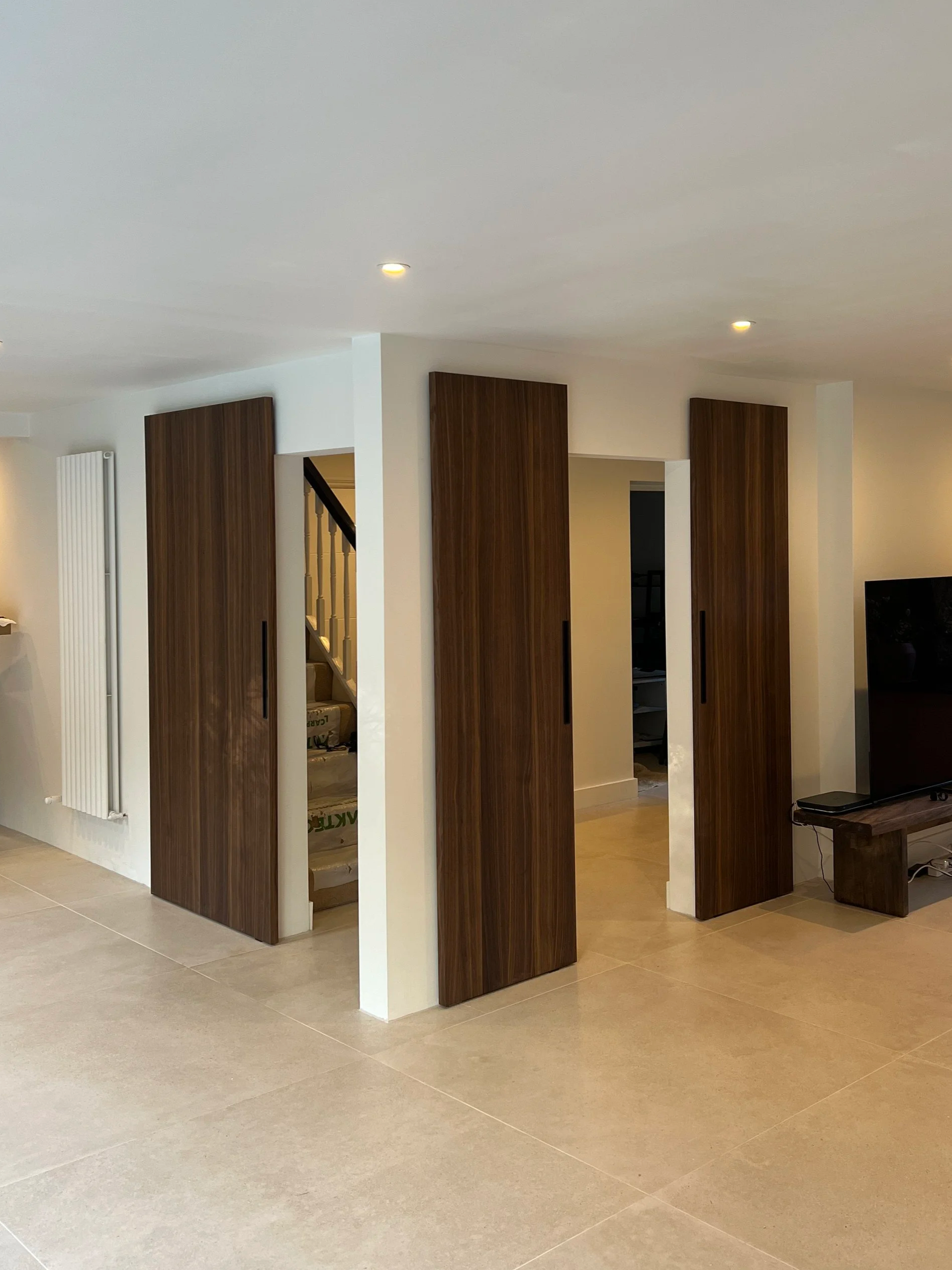 Interior of a home under renovation with partial wall dividers and wooden panels, a staircase, and a television on a wooden stand.