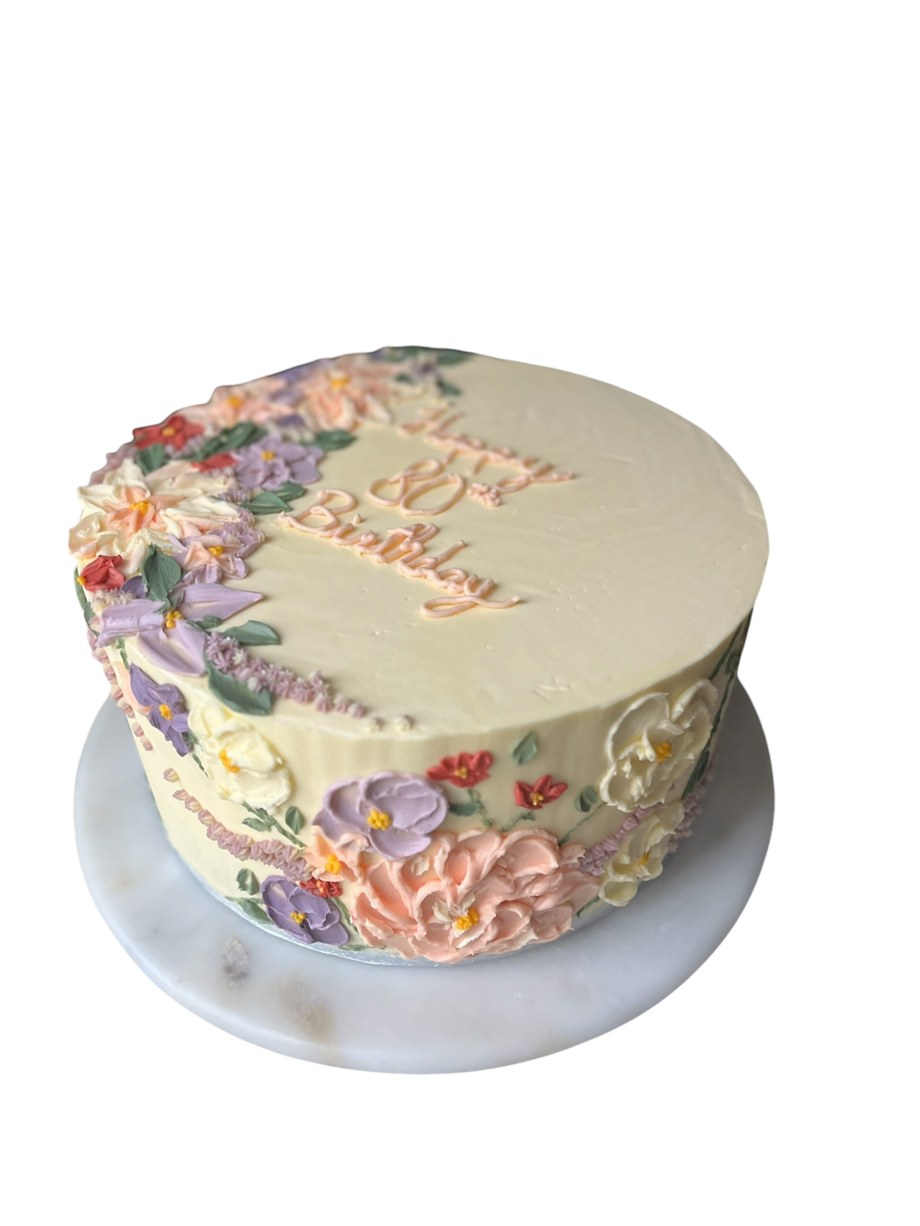 A round cake decorated with pastel-colored flowers and words written on top, placed on a white marble cake stand.