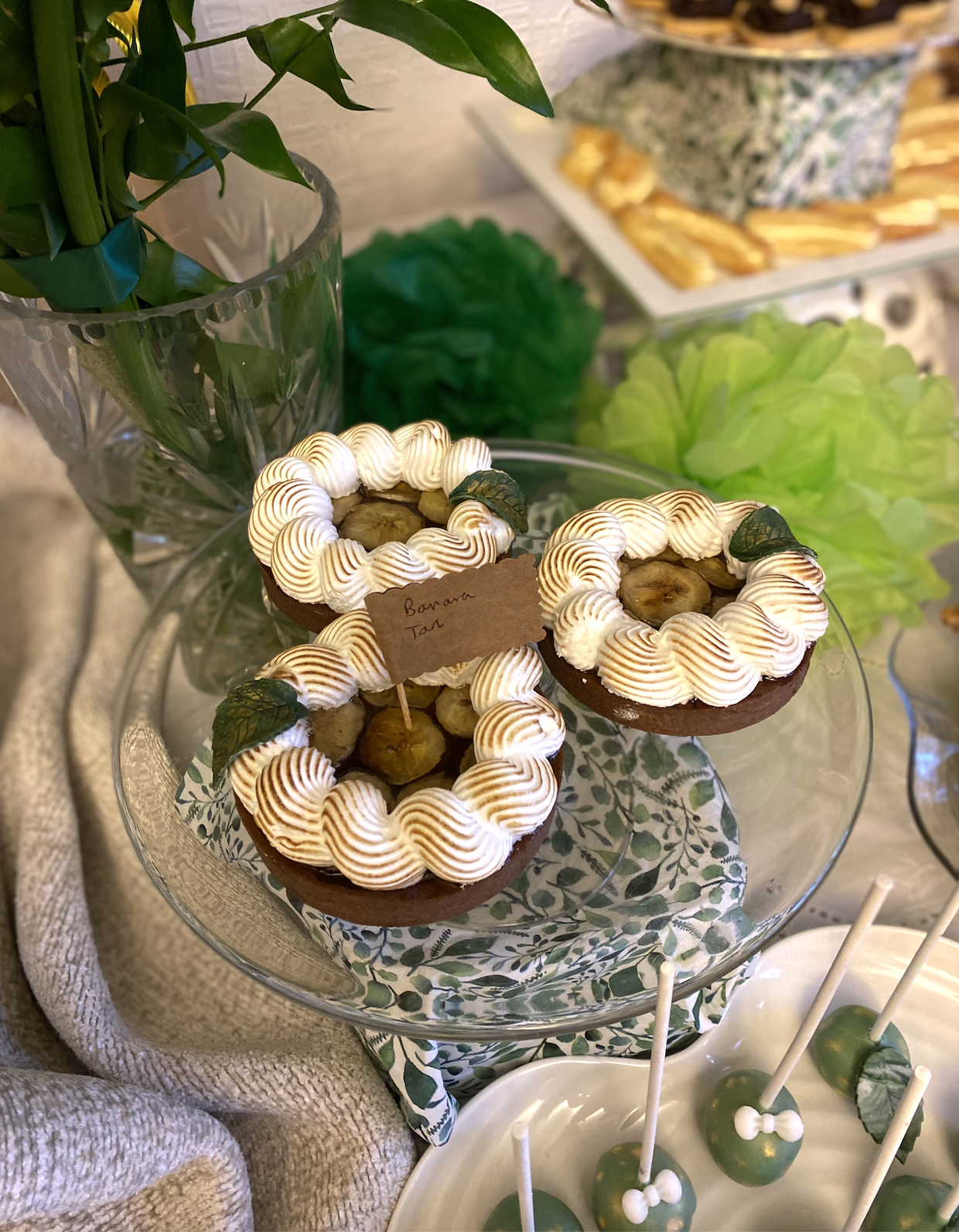 Three banana tarts with whipped cream, banana slices, and mint leaves on a glass cake stand.