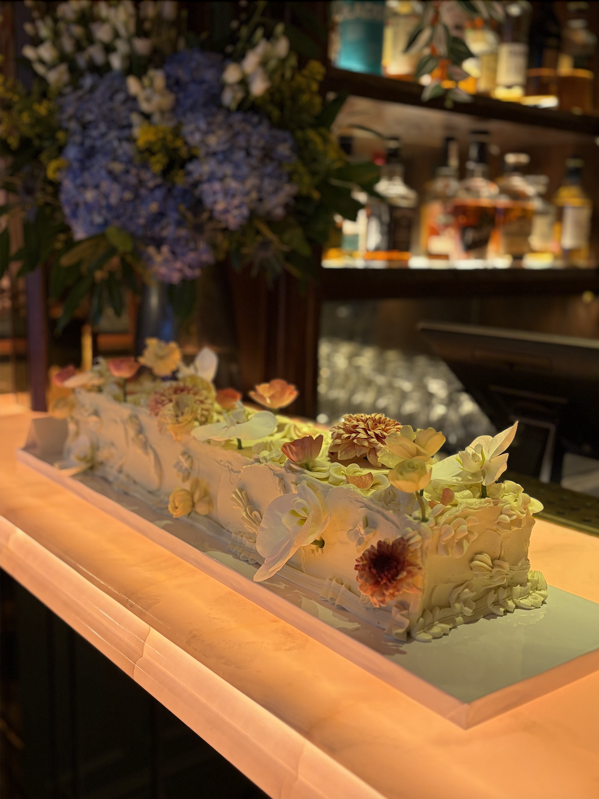 Rectangle long flower cake with delicate piping details displayed on a lit glowing bar