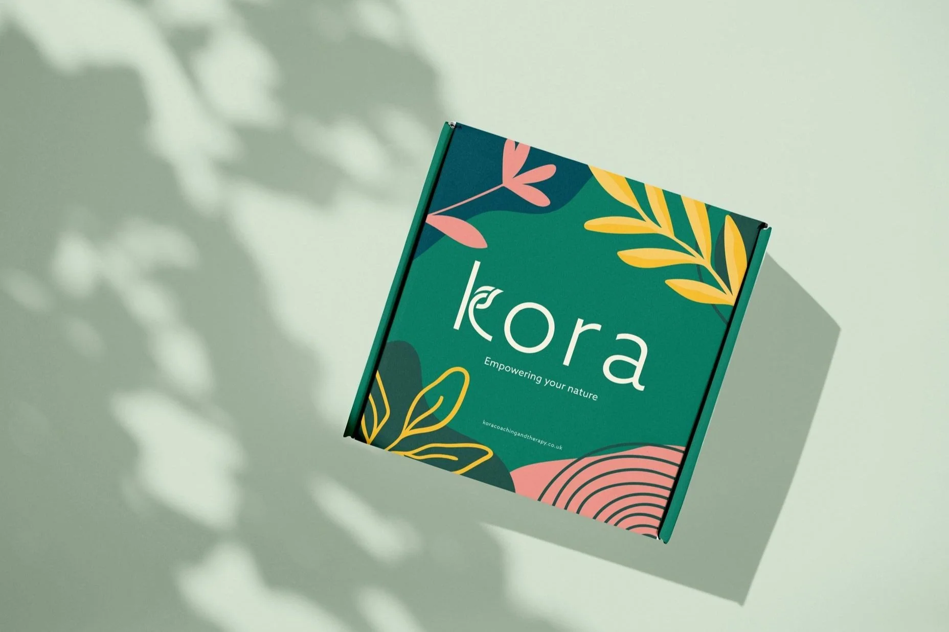 A green Kora box with pink, yellow, and dark green accents, featuring the beige Kora logo in the center.