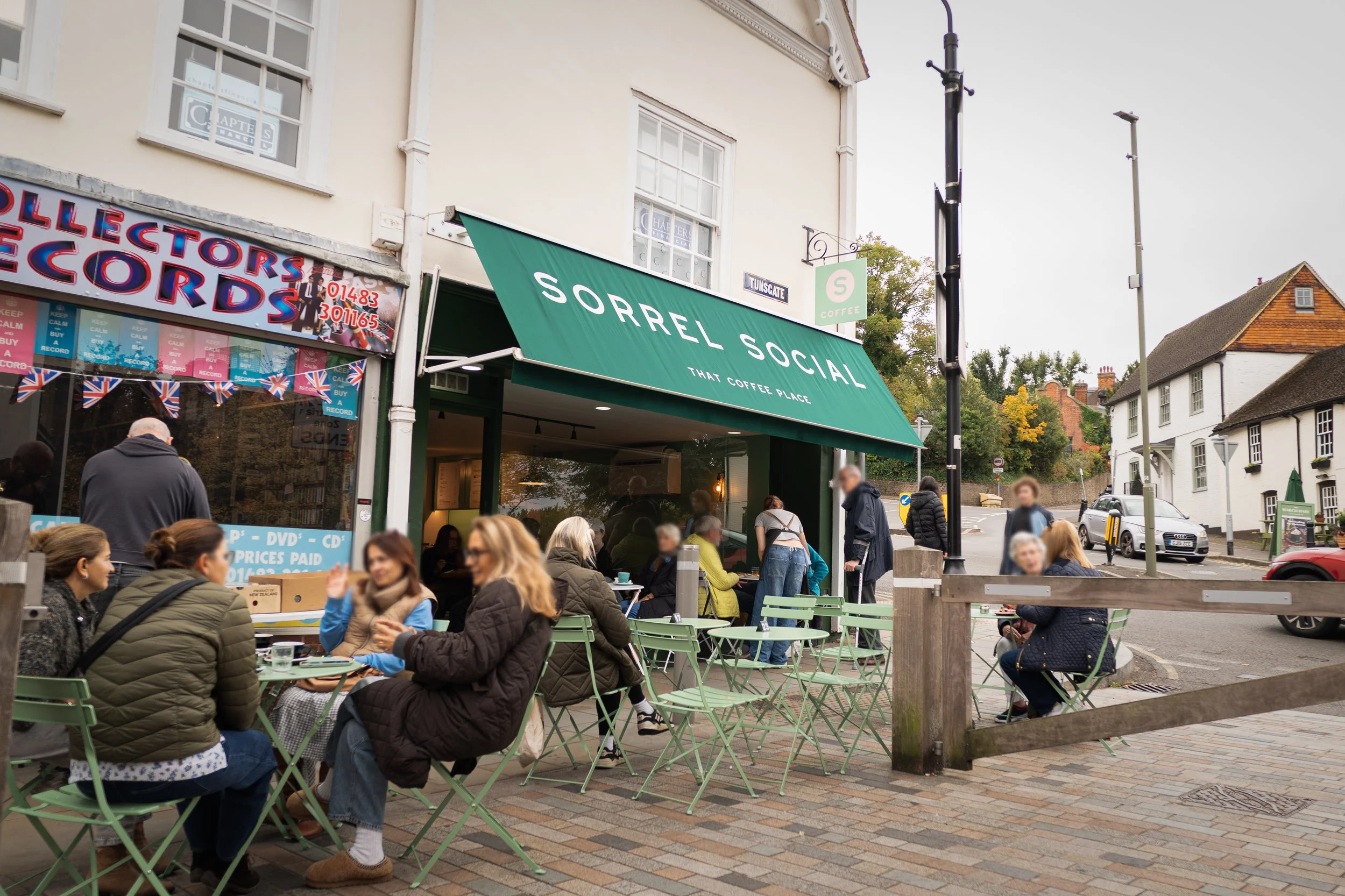 A busy picture of the front of the Sorrel Social coffee shop. Customers are sat under the green canopy with the white sorrel social logo on.
