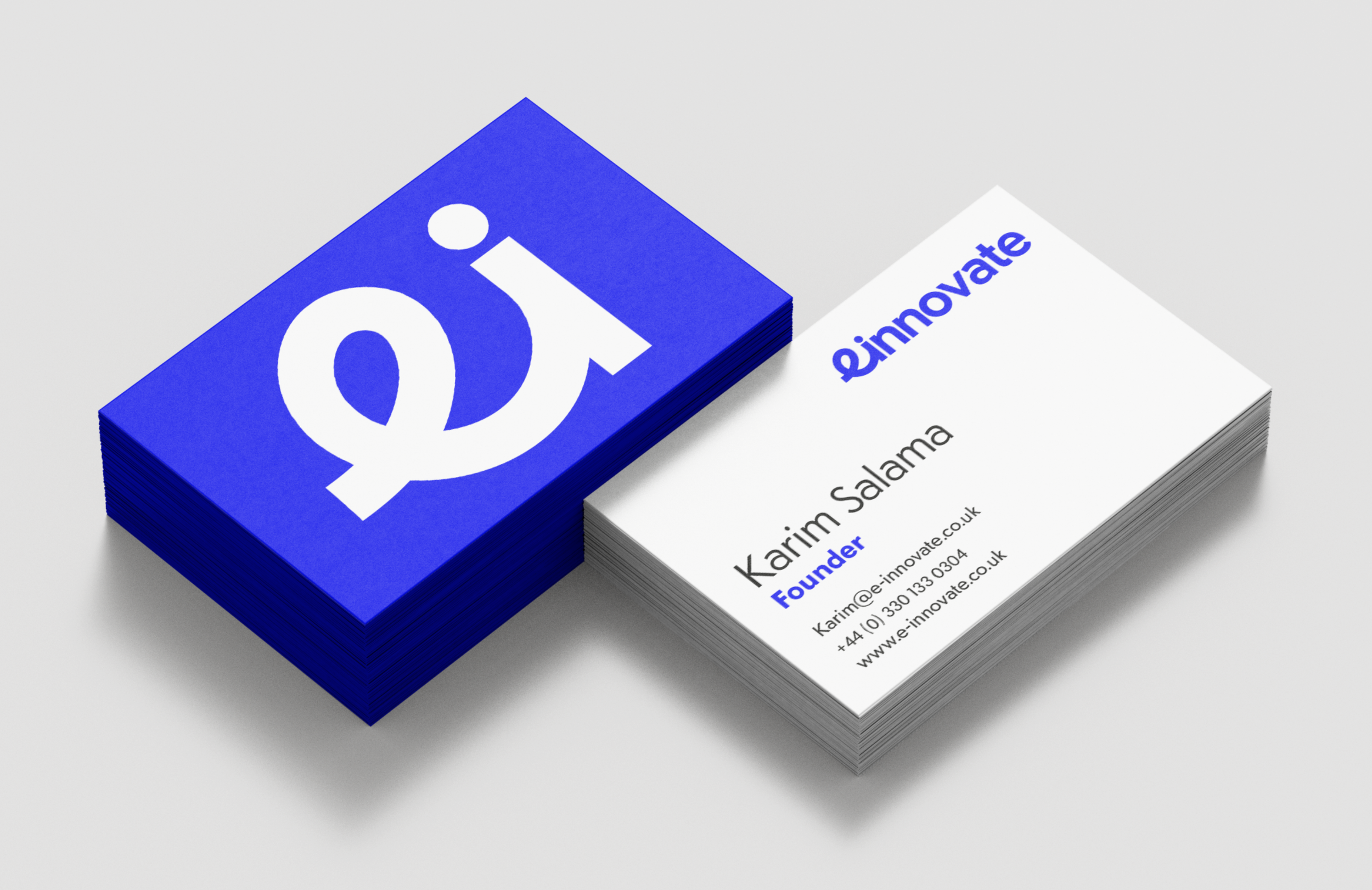 A set of einnovate business cards arranged on a white surface. One side of each card is bright blue featuring the einnovate ‘ei’ logo, while the reverse side is white displaying the cardholder’s name and contact details.