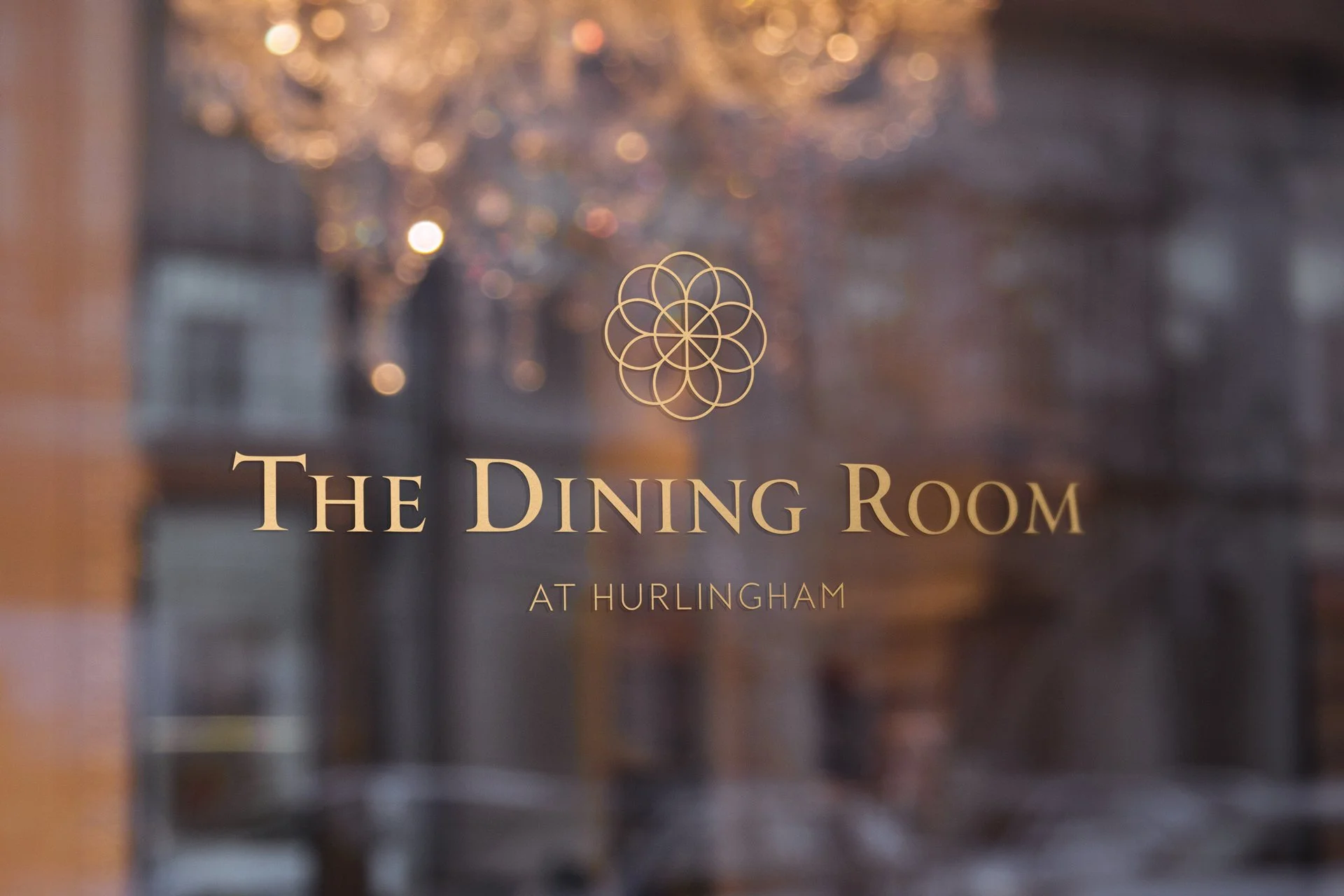An elegant gold sticker reading “The Dining Room, at Hurlingham” is placed on a window, adding a refined touch to the setting.