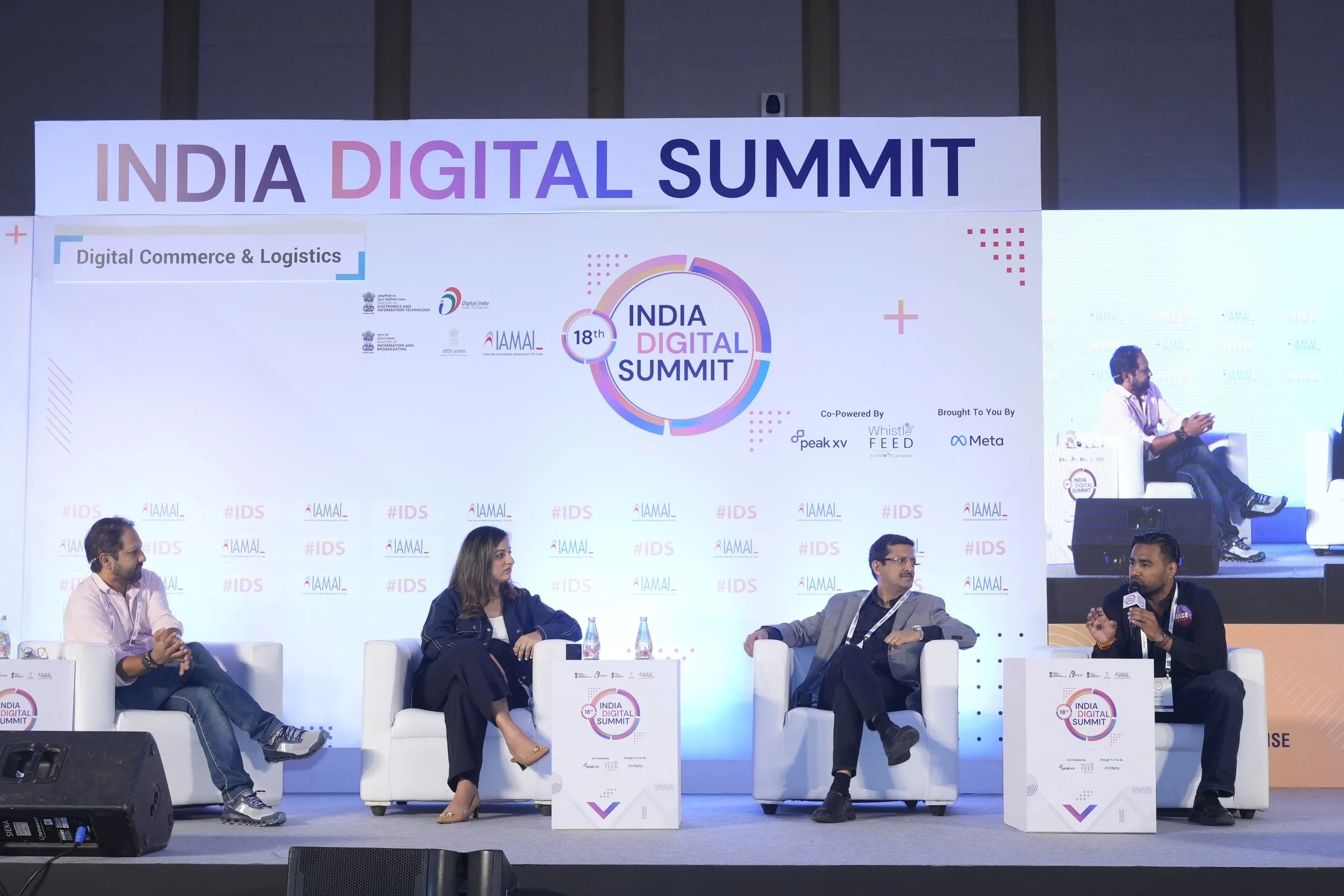 Four individuals seated on stage at India Digital Summit, engaged in panel discussion, with a large backdrop displaying the event logo and sponsors.