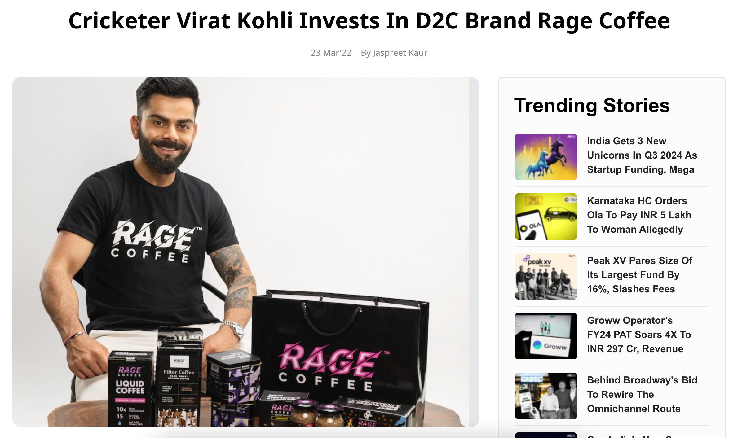 Man with a beard wearing a black Rage Coffee T-shirt, smiling, sitting with Rage Coffee products on a table, including liquid coffee cartons, filter coffee packs, and a Rage Coffee bag.