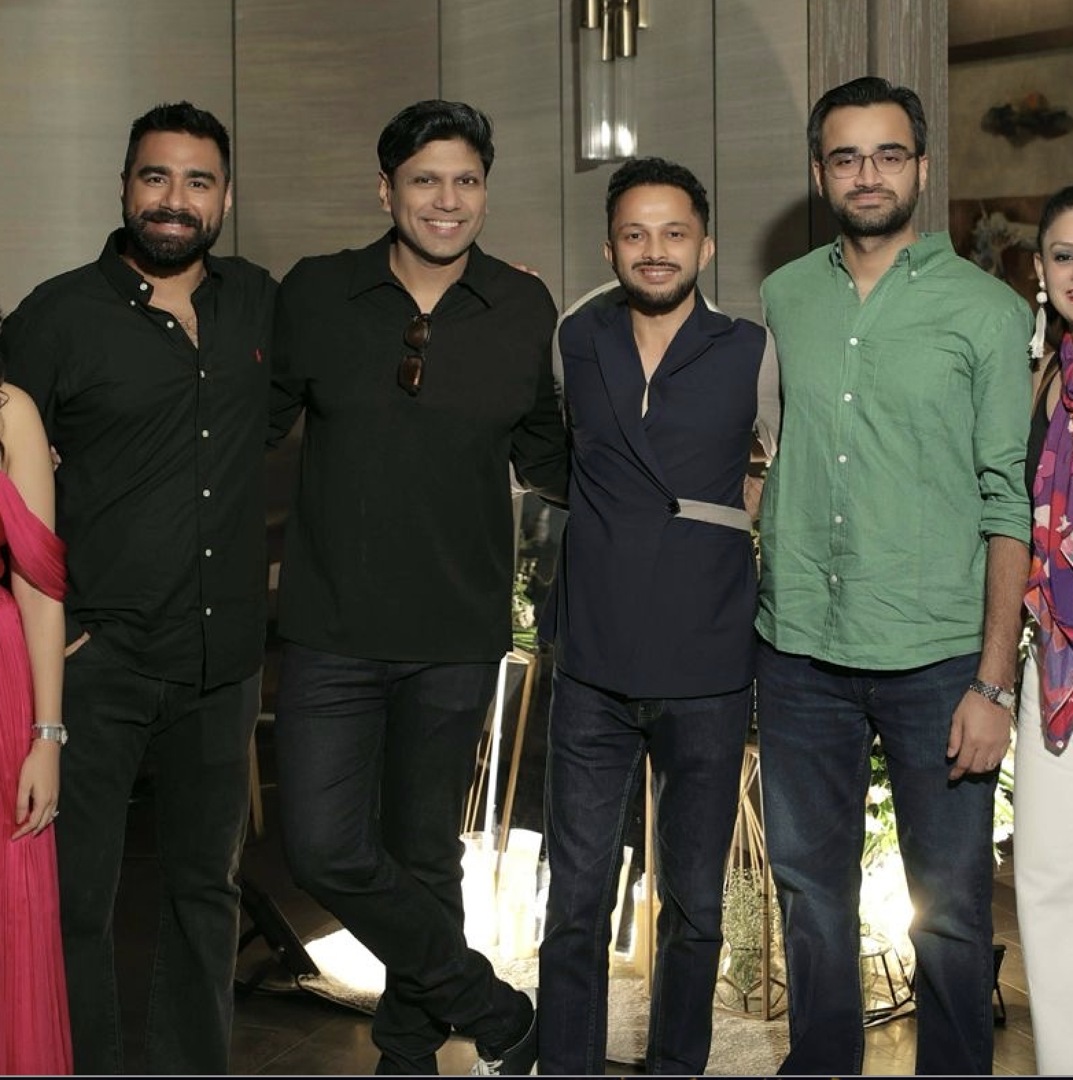 Group of five men standing together indoors, smiling, in casual and semi-formal attire.