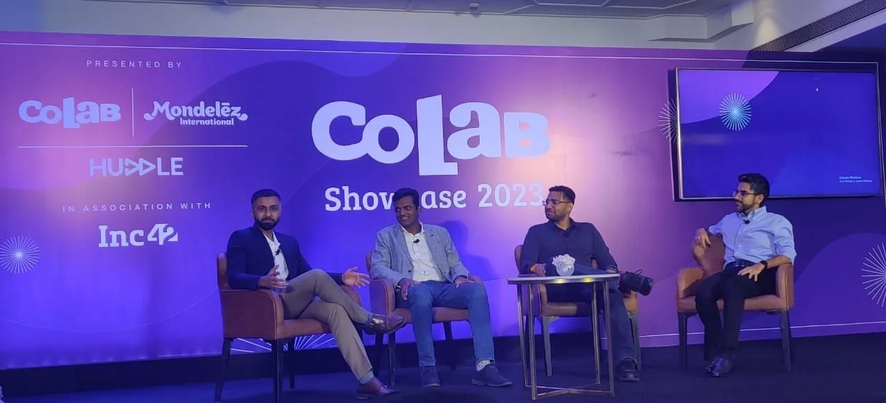 Four men sitting on stage chairs at CoLab Showcase 2023 event, with a large backdrop displaying logos of CoLab, Mondelēz, and Inc42.