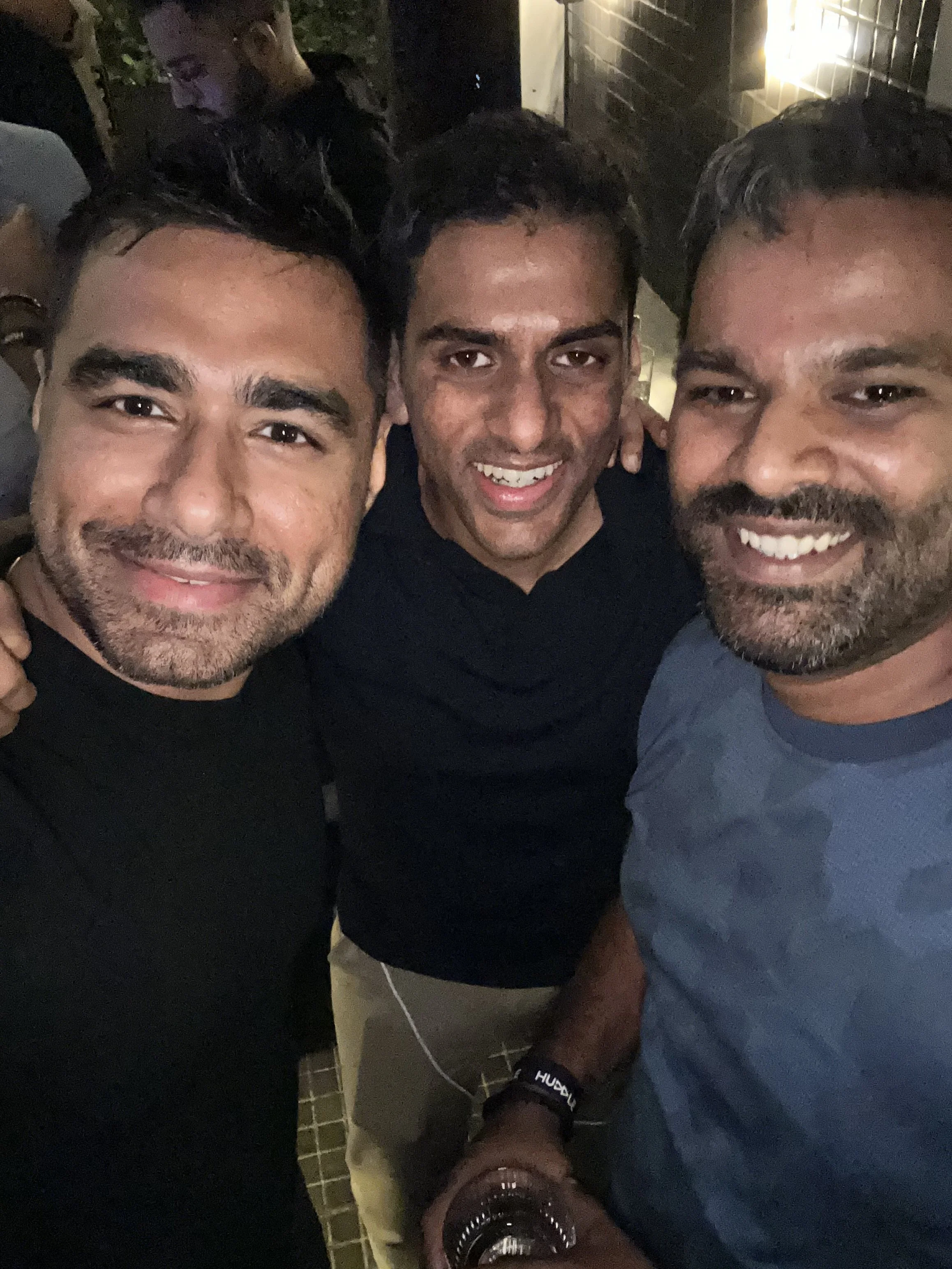 Three men taking a selfie together outdoors at night, smiling and enjoying each other's company.