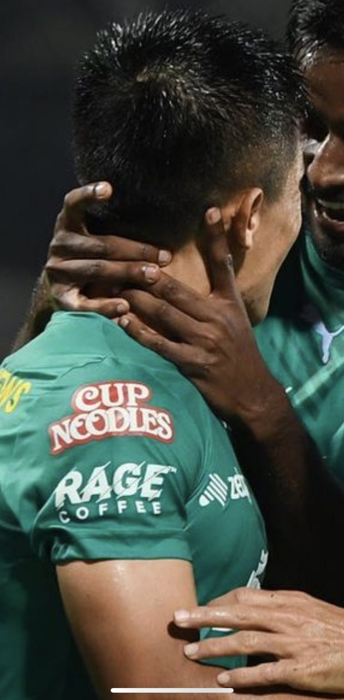 Two athletes in green jerseys share an emotional moment, embracing and kissing each other during a sports event.