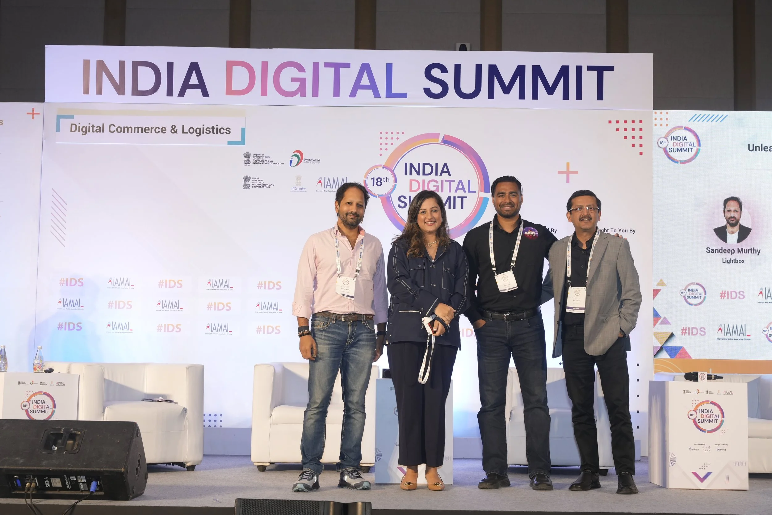Four people standing on stage at the India Digital Summit, smiling, with a large backdrop behind them displaying event logos and the text 'India Digital Summit'.