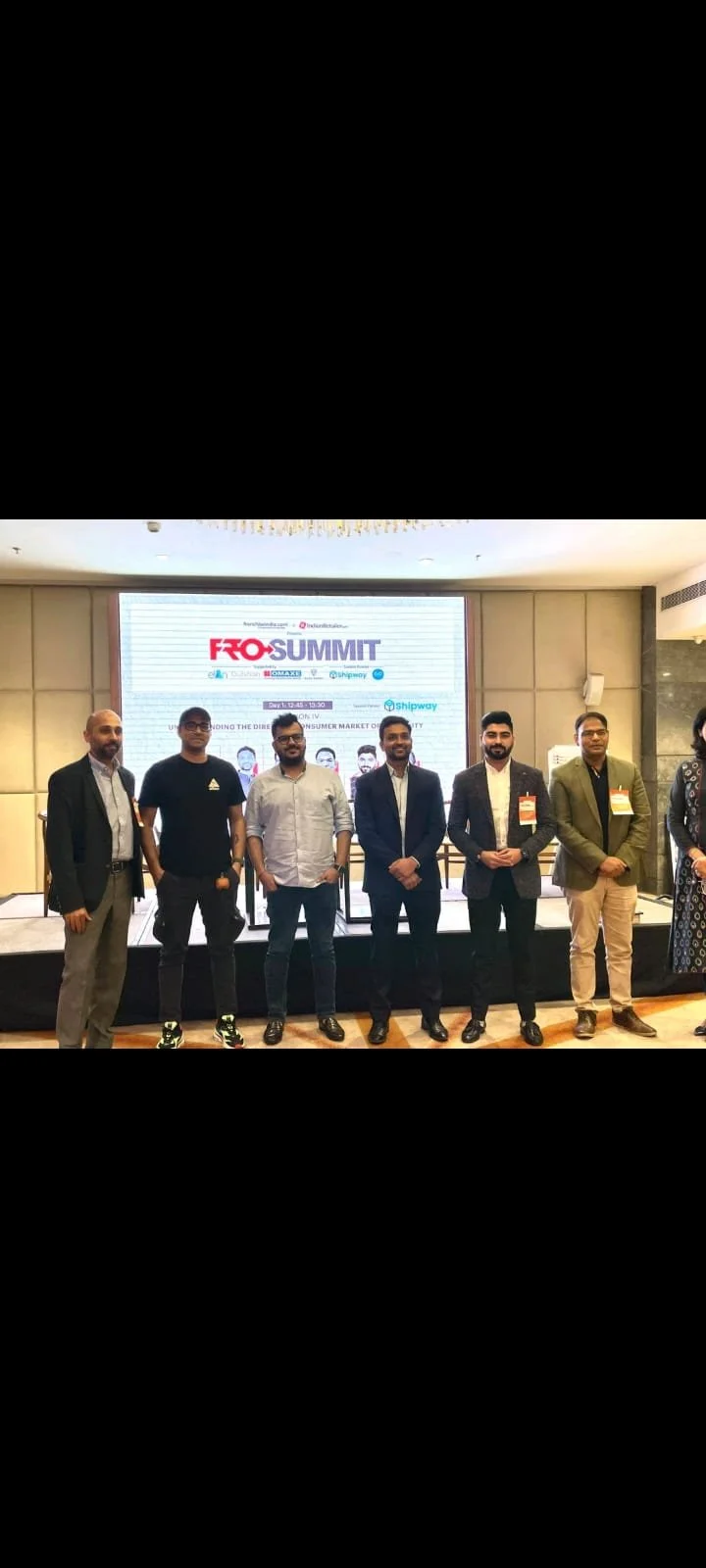 Group of six men standing in front of a presentation screen at the FRO Summit, with conference badges and formal attire.