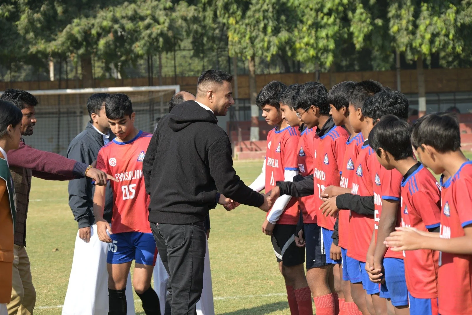 A group of young male soccer players in red jerseys lined up on a field, receiving awards or recognition from adults during a ceremony.