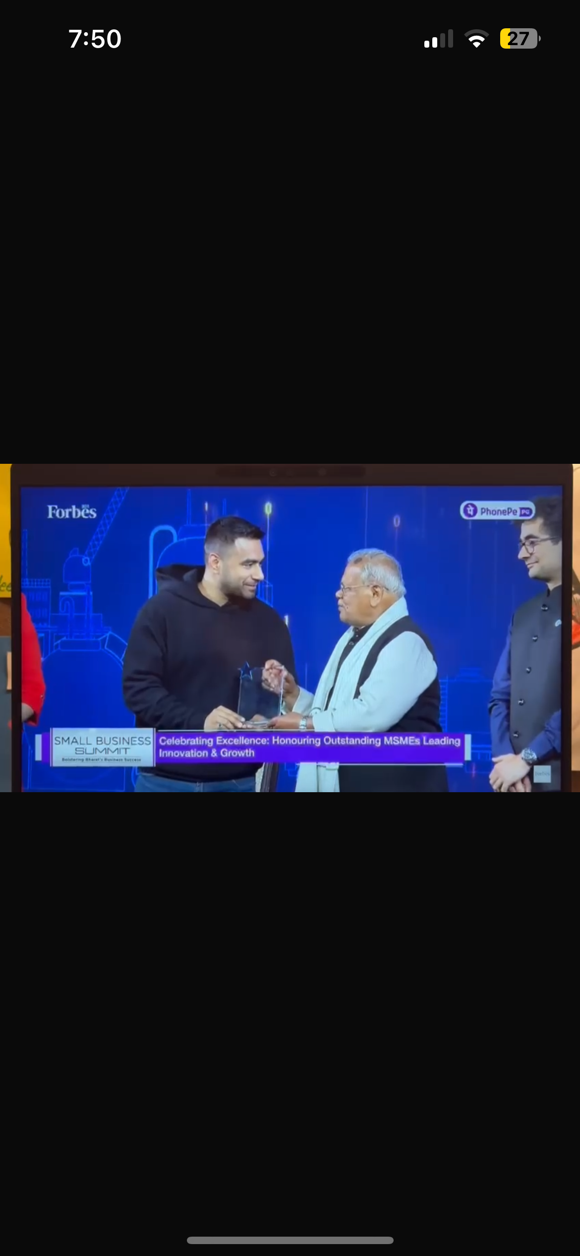 Two men shaking hands on stage during an awards ceremony at a small business summit, with a third man standing nearby. A large screen in the background displays the words 'Forbes' and the event's theme related to honoring outstanding MSMEs.