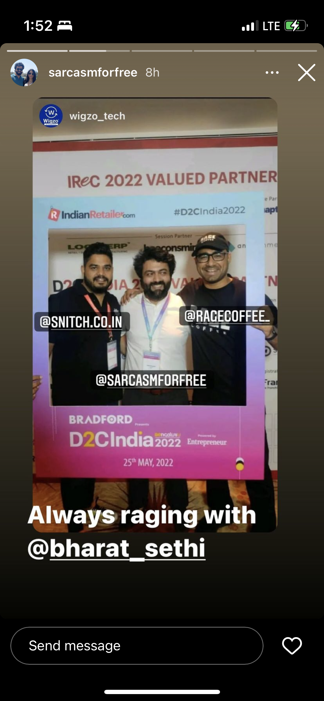 Photo of three men at D2C India 2022 event, standing behind a pink and white sign with event details. They are smiling, and each has a tag with their social media handle. The background shows part of the event banner with sponsor logos and text.