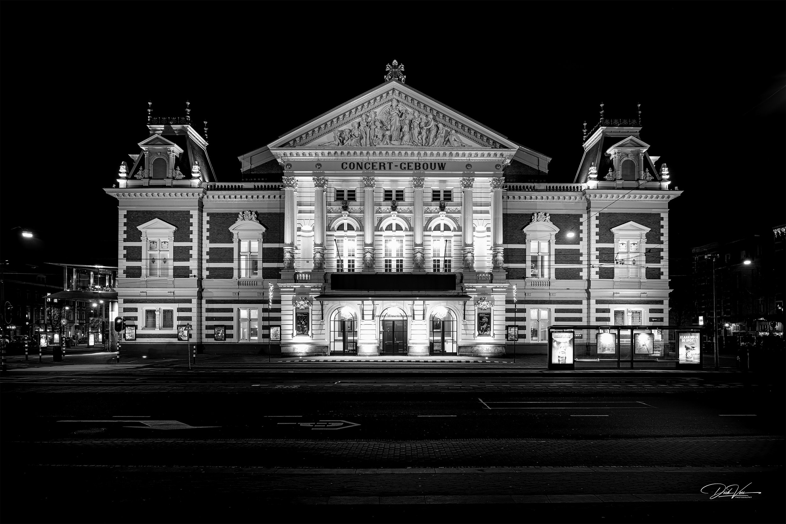 Schwarz-weiß-Foto eines beleuchteten Konzerthauses bei Nacht mit klassischer Fassade und imposanten Säulen.