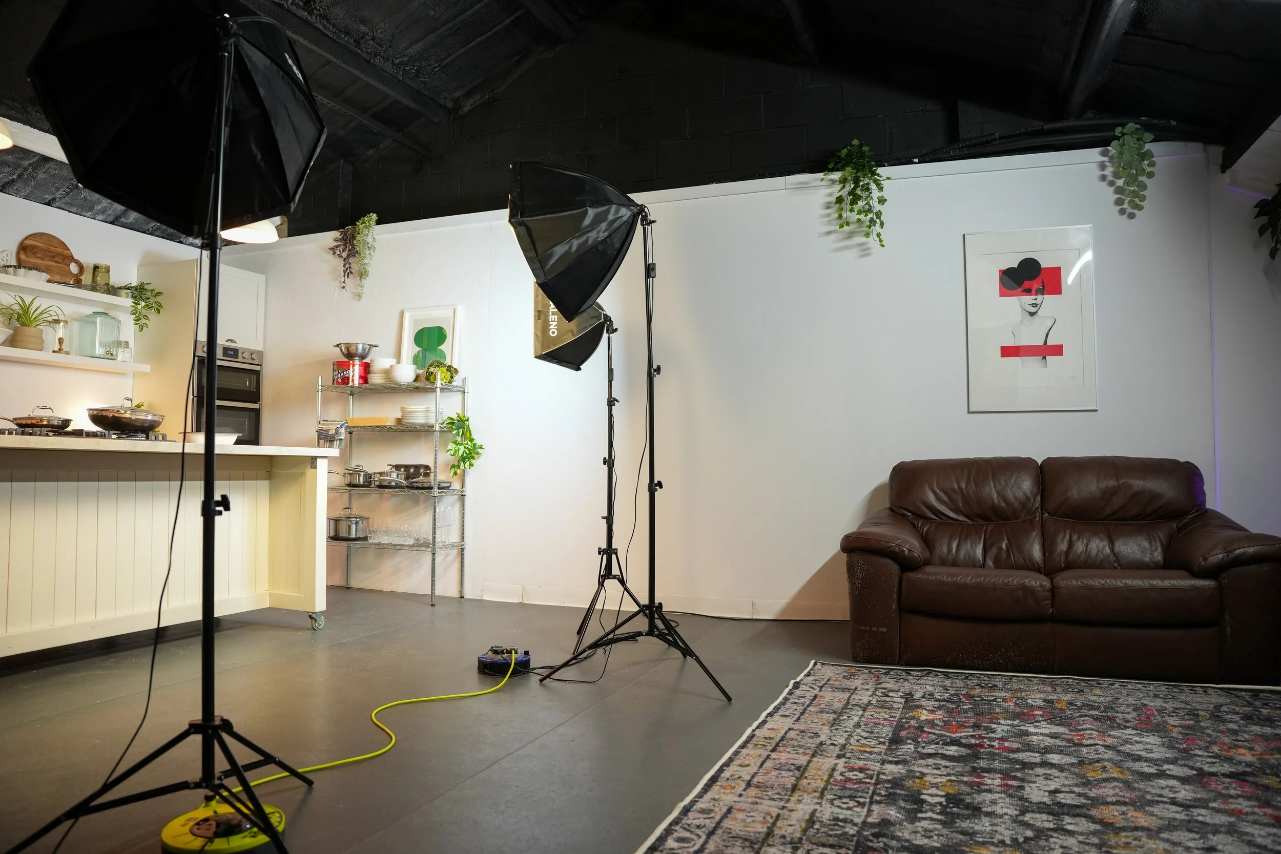 Encore Kitchens' studio kitchen set up for a photo shoot, with softbox lighting, a fitted kitchen island, open shelving, and a lounge area with leather sofa and rug.