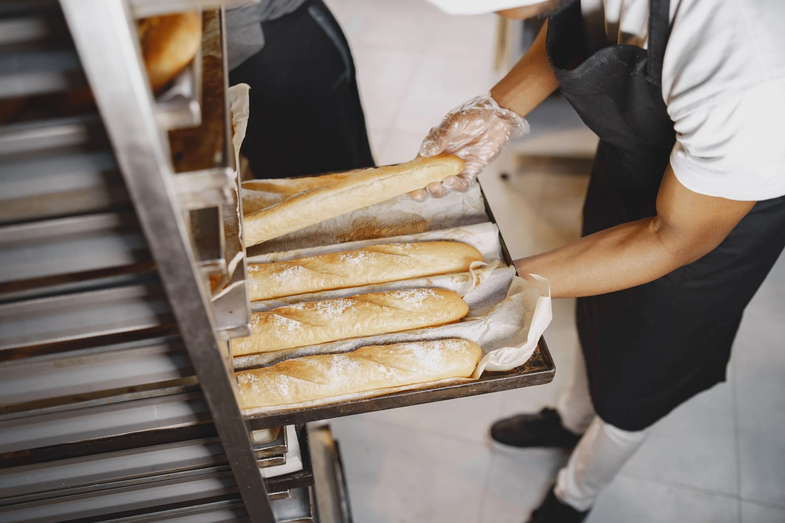 Kitchen staff handling a tray of bread in a high-volume production kitchen