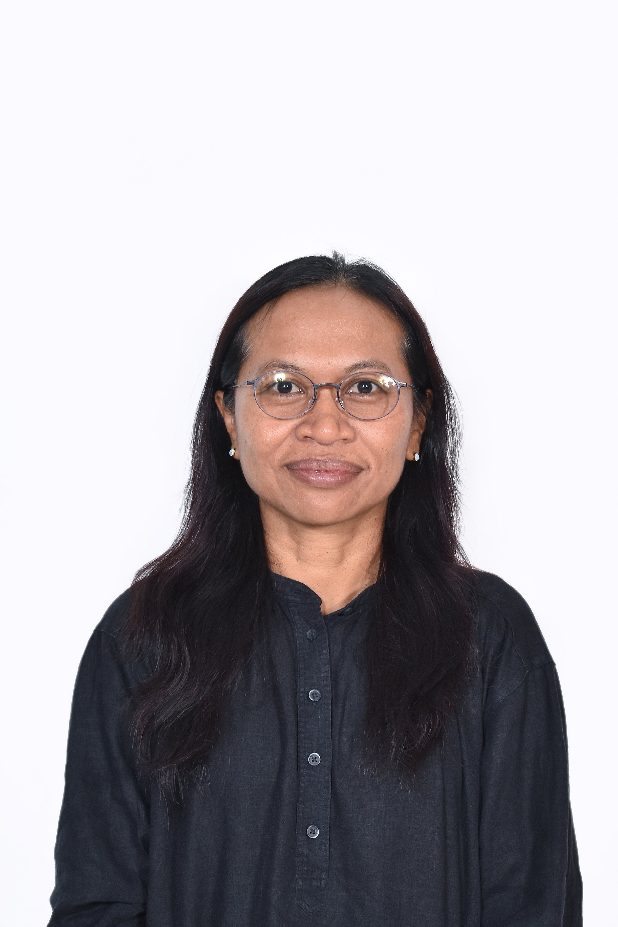 A woman with long dark hair, wearing glasses and a black button-up shirt, smiling in front of a plain white background.