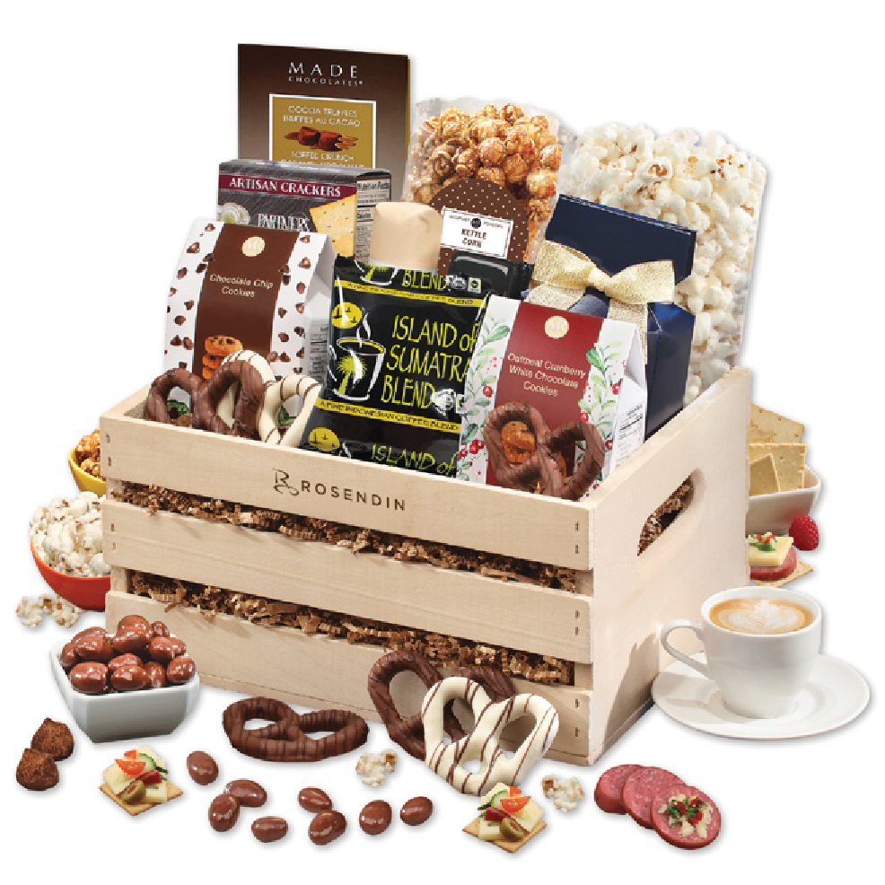 A wooden gift basket filled with chocolates, snacks, and a bowl of popcorn, surrounded by additional treats and a cup of coffee.
