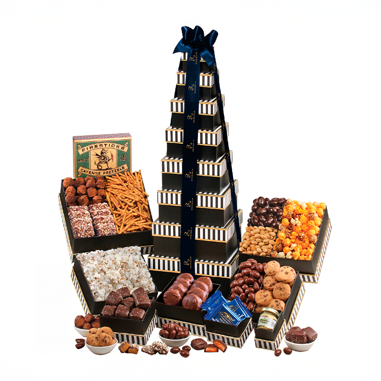 A tower of stacked chocolate boxes with a large blue ribbon on top, surrounded by various chocolates, cookies, and snacks including pretzels, popcorn, nuts, and candy.