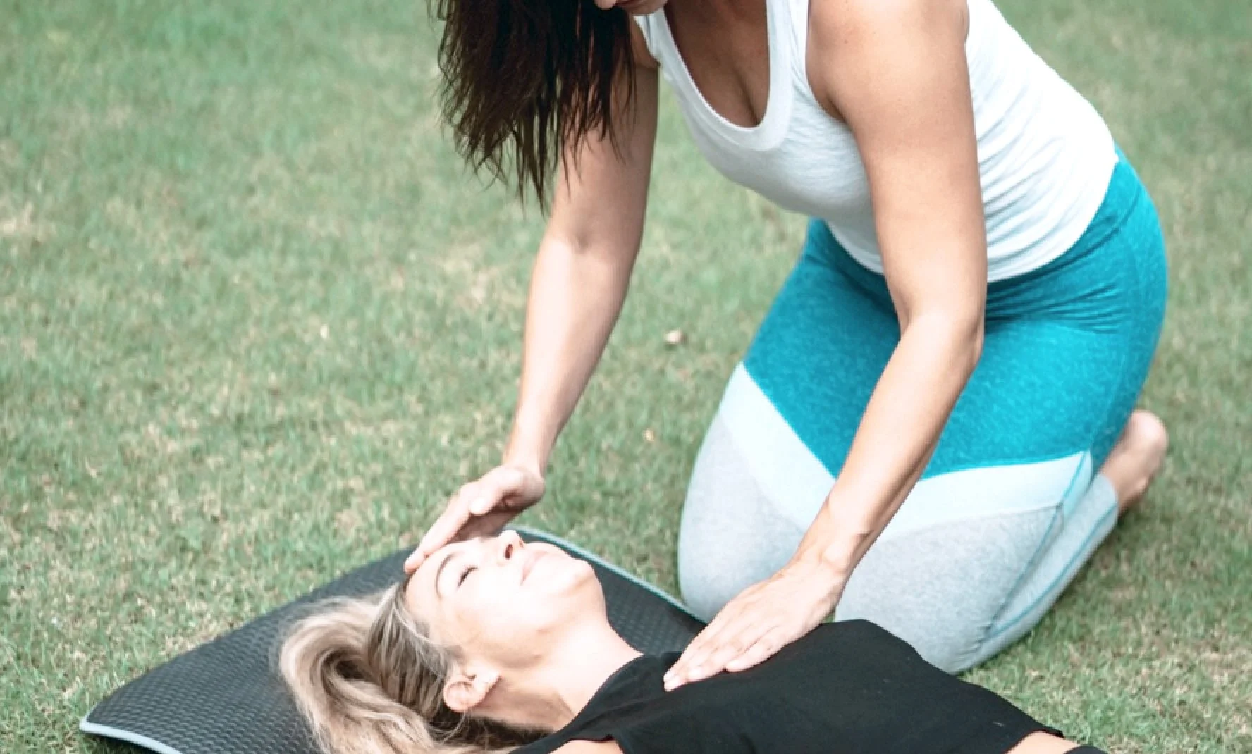 Woman performing CPR on a woman lying on a yoga mat outdoors.