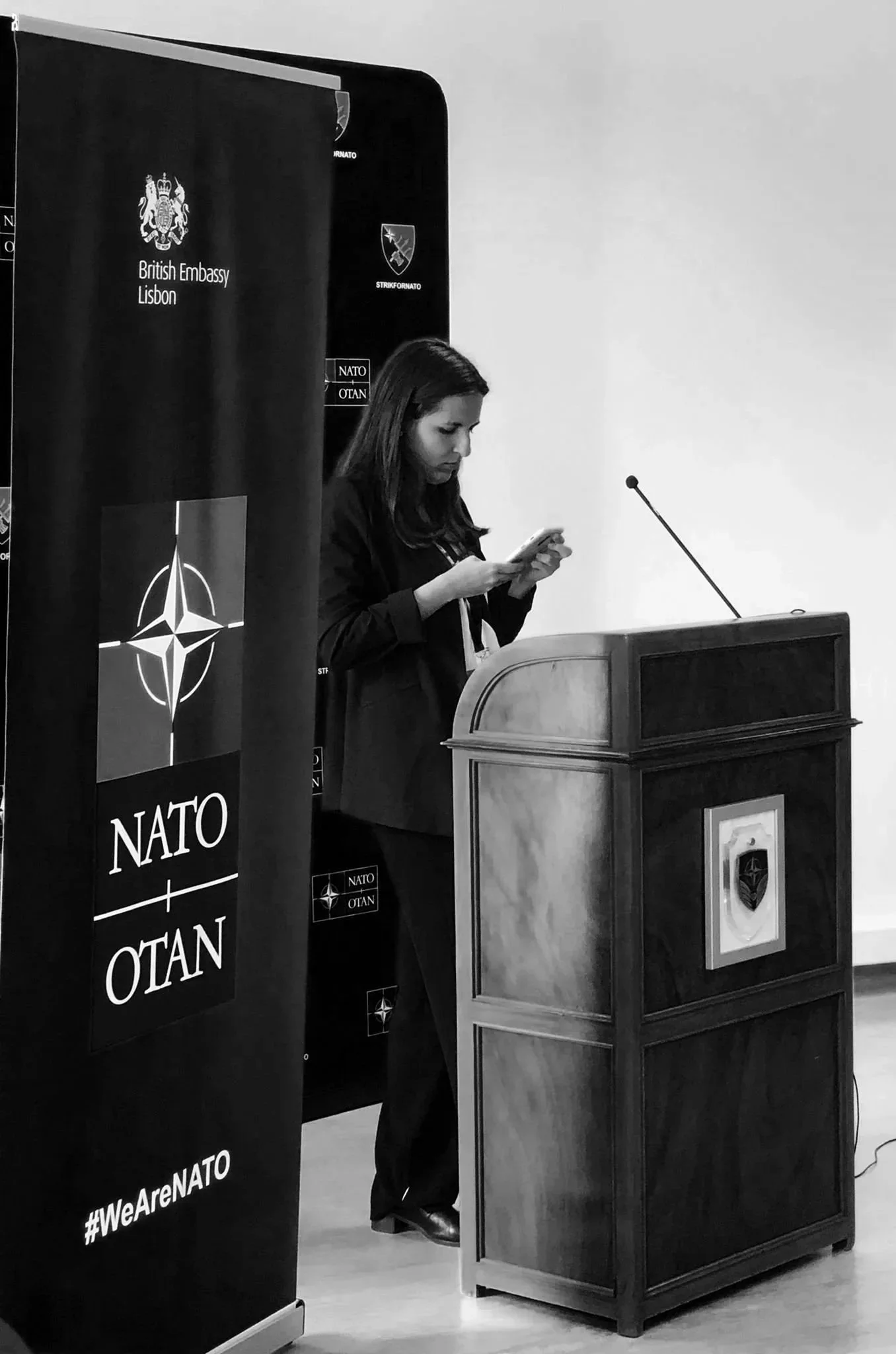 maria luísa moreira foreign affairs analyst standing next to the NATO/OTAN and the British Embassy Lisbon banner