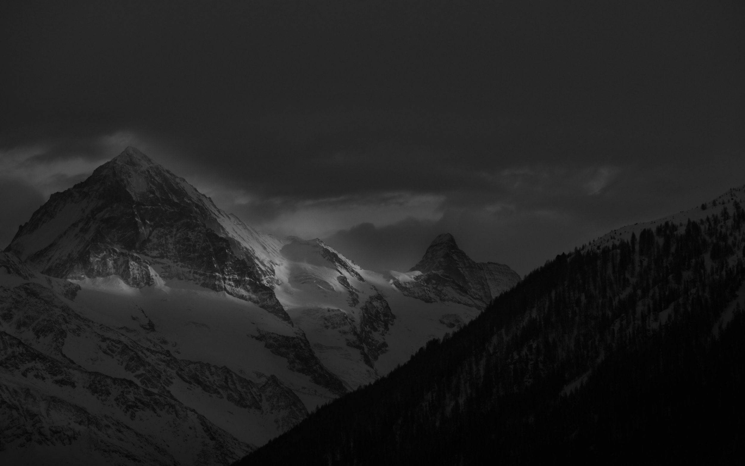 Snow-covered mountain peaks under dark cloudy sky