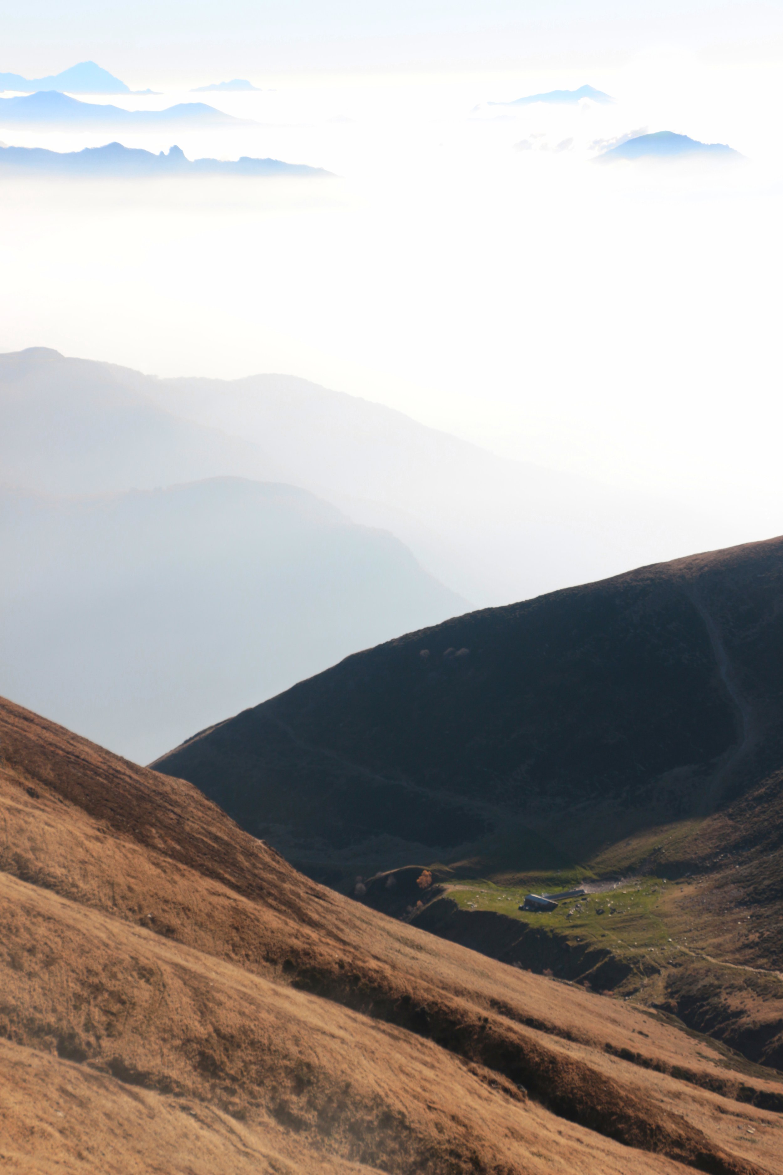 Mountain landscape with rolling brown hills, rocky peaks, and distant misty mountain ranges in the background.