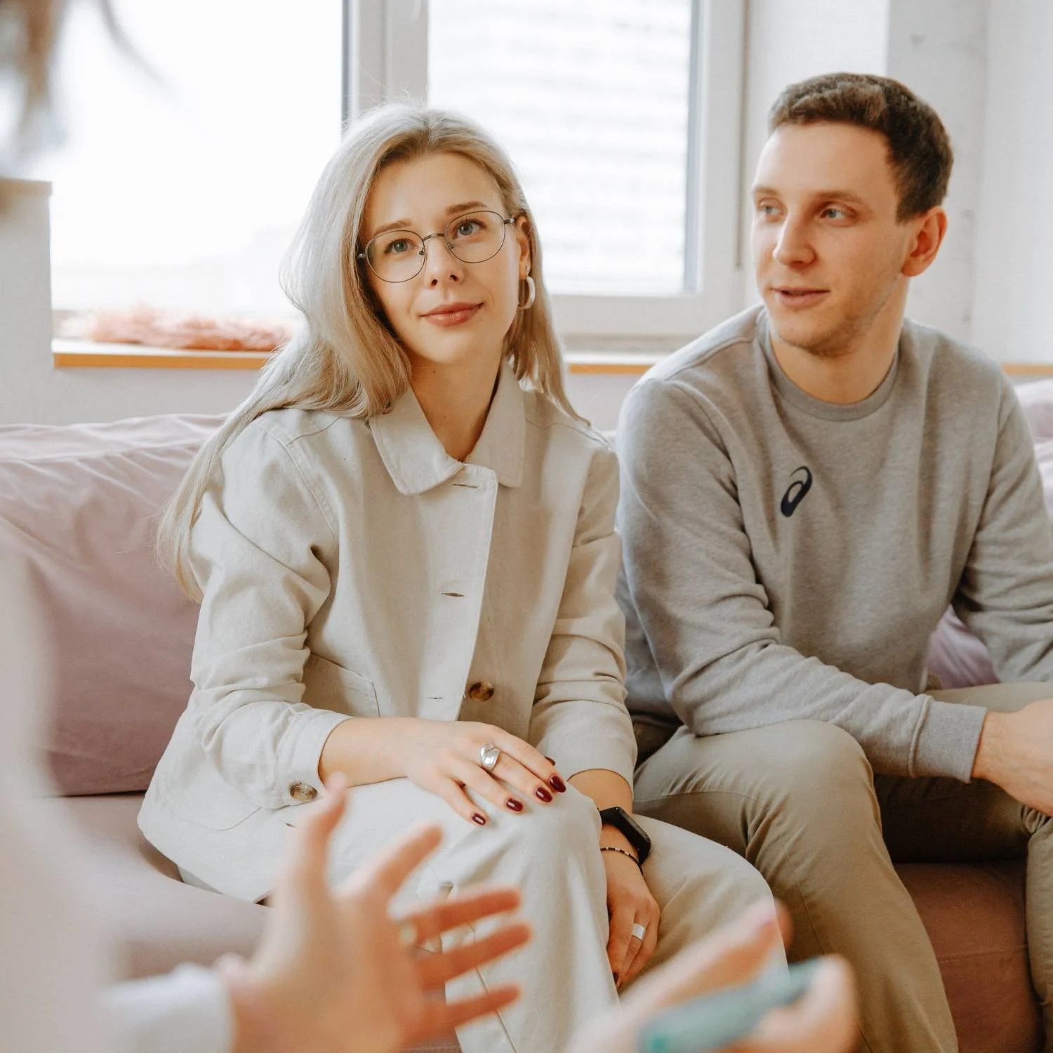 A woman and man sitting on a couch, engaged in conversation with someone off-camera.
