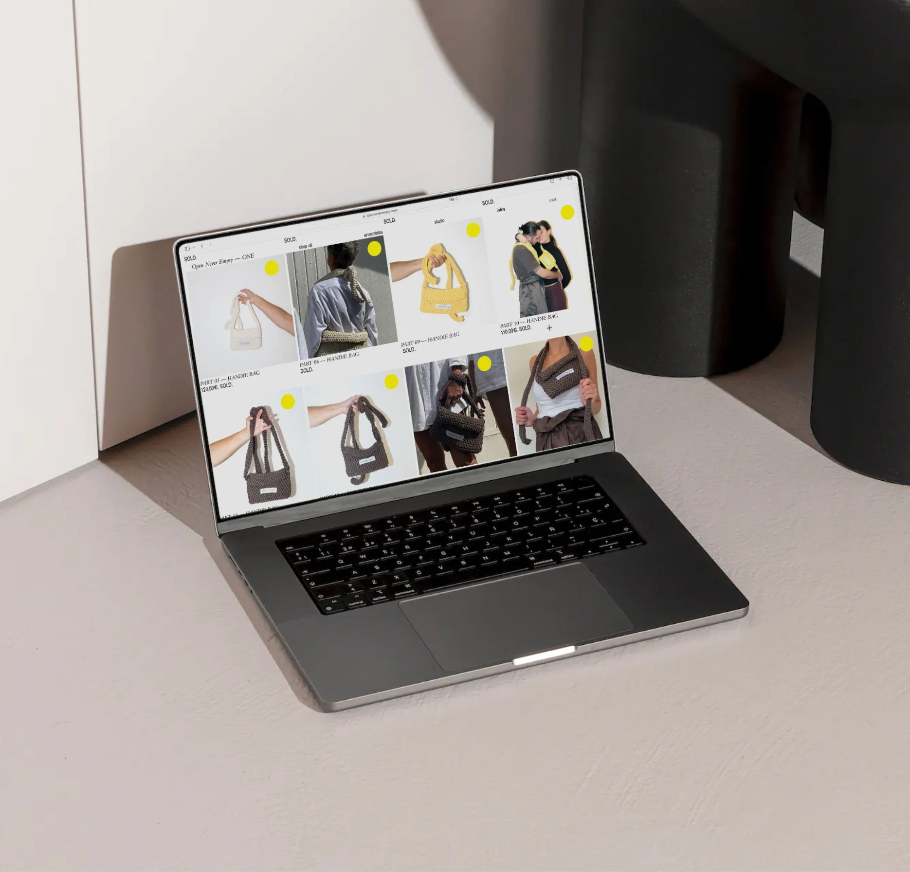 A laptop on a beige surface displaying an online store with images of handbags and women modeling them.